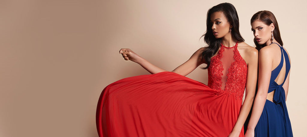 Two teen girls, one in a navy prom dress and one in a red prom dress with the skirt flared out.