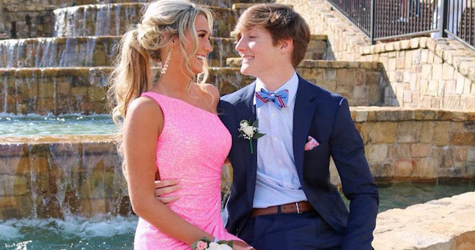 Teen girl in one-shoulder pink prom dress looking at her date in a blue suit.