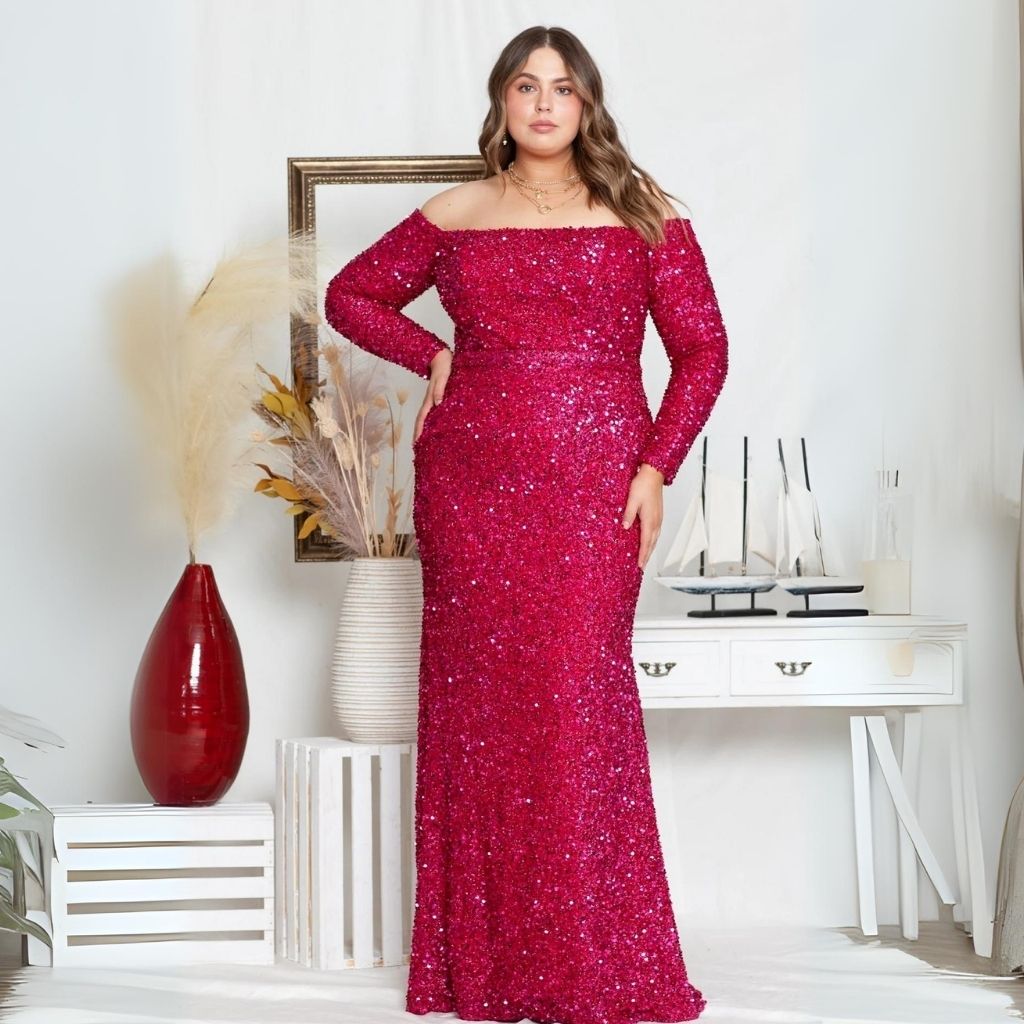 In an off-the-shoulder plus-size red sequin dress with long sleeves, a woman poses in front of white furniture.