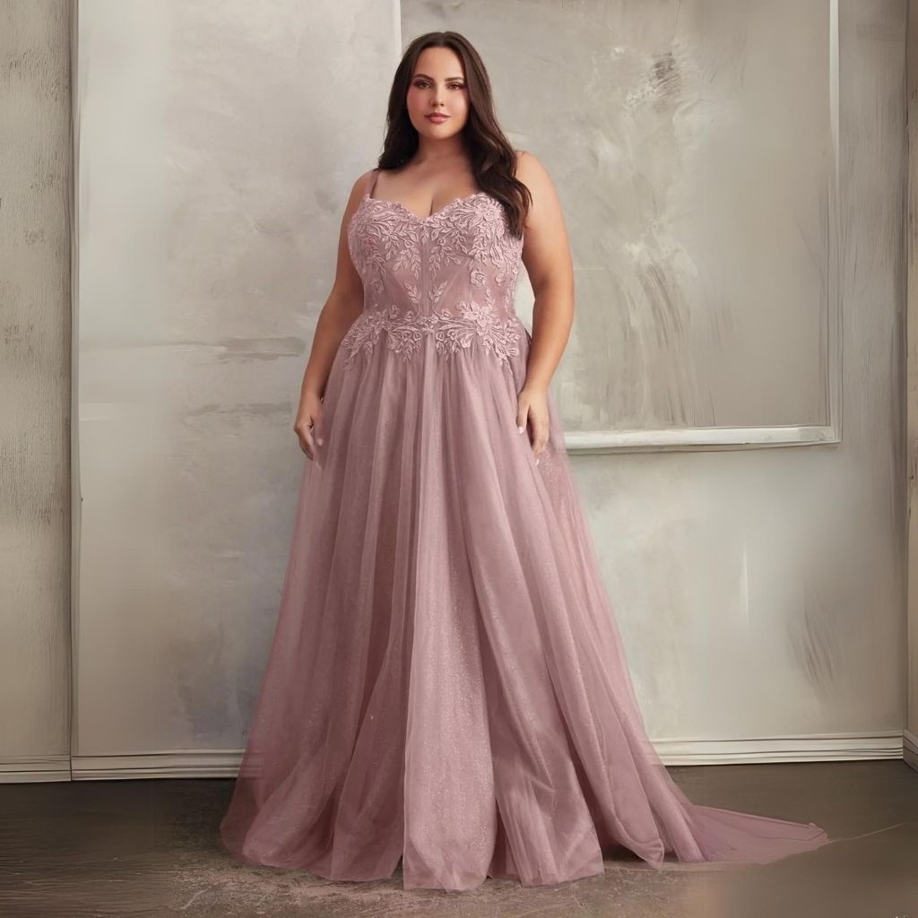 In front of a marble wall, a woman stands wearing a dusty rose pink plus-size a-line formal dress.