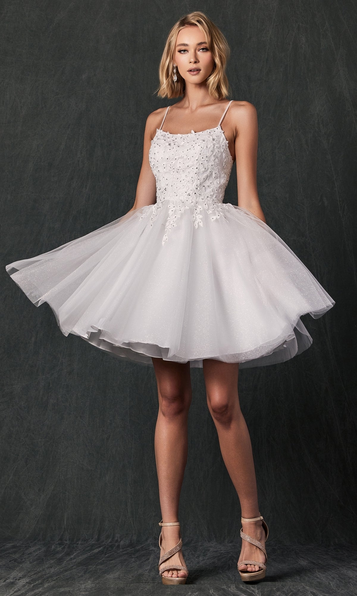 Woman wearing the Embroidered-Corset Babydoll Homecoming Dress 860, a short white cocktail dress with floral embroidery and spaghetti straps, standing in front of a dark textured background.