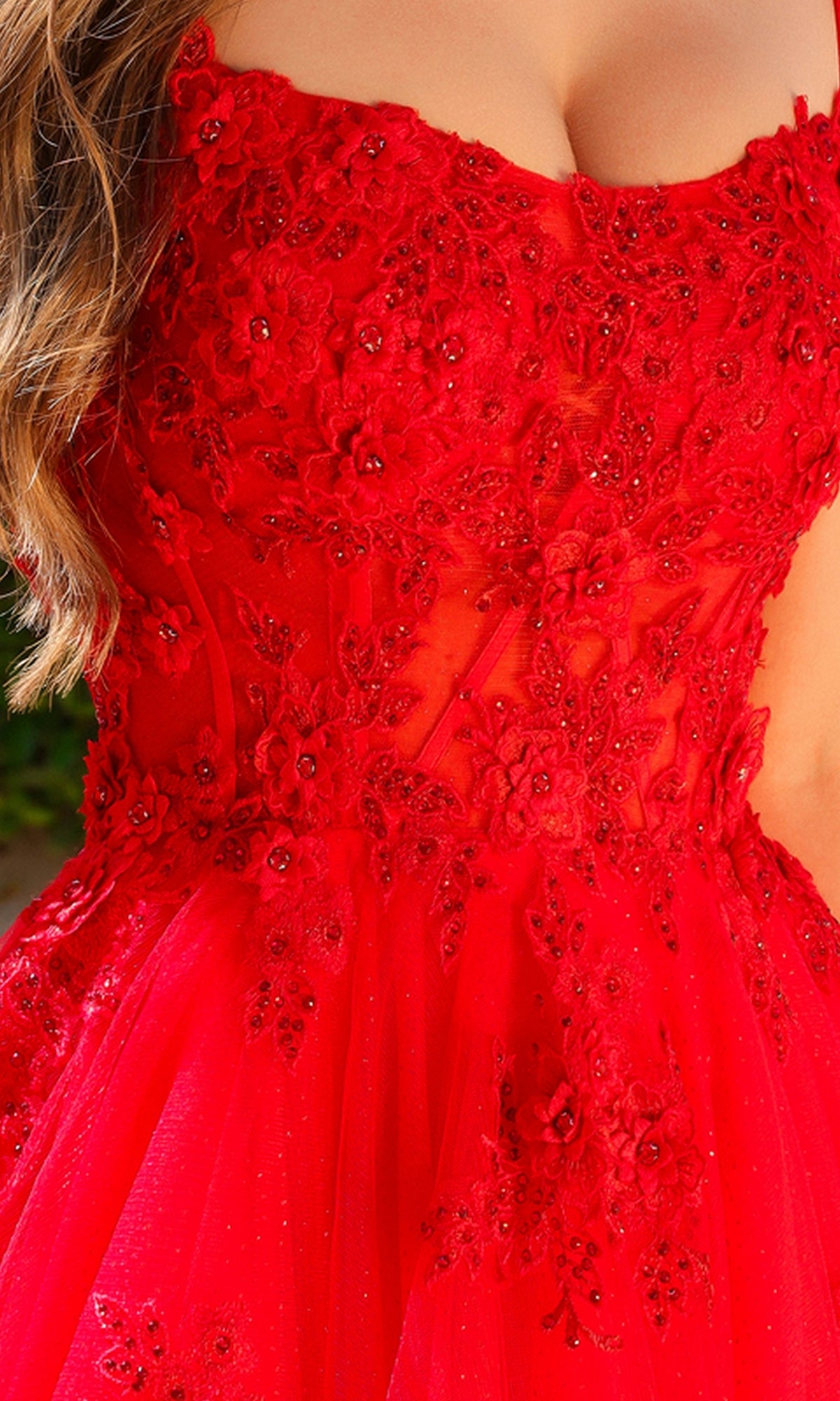 A close-up of a woman wearing the Embroidered-Tulle Long A-Line Prom Ball Gown 7035, featuring red tulle, floral embroidery, sheer panels, and intricate bead detailing.