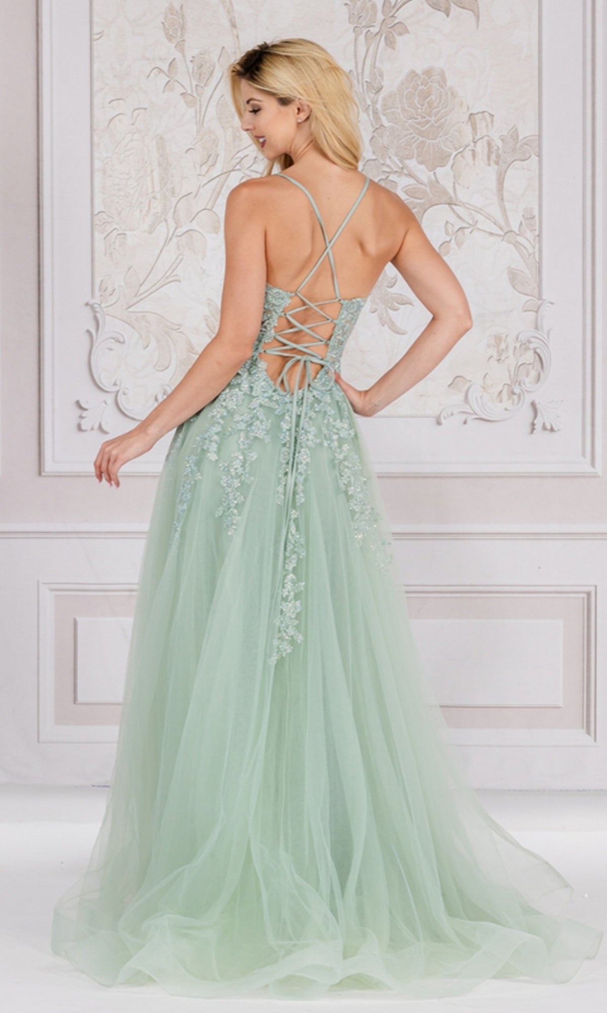 A woman wears the Floral-Embroidered Long A-Line Prom Dress TM1006 in light green, featuring a lace-up back and delicate floral embroidery, as she stands before a decorative wall.