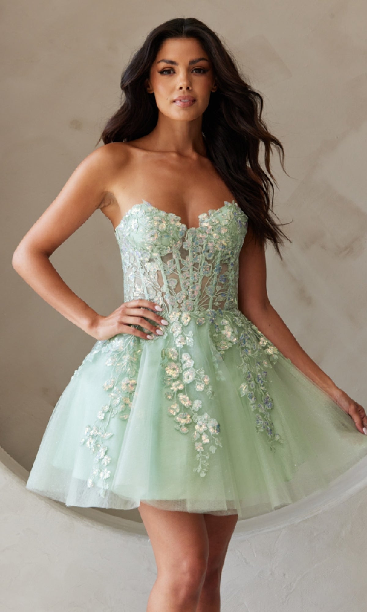 A woman wears the Strapless Short Pastel Homecoming Dress BZ9024S—light green, floral-embroidered with a fitted bodice and flared tulle skirt—standing against a neutral background.