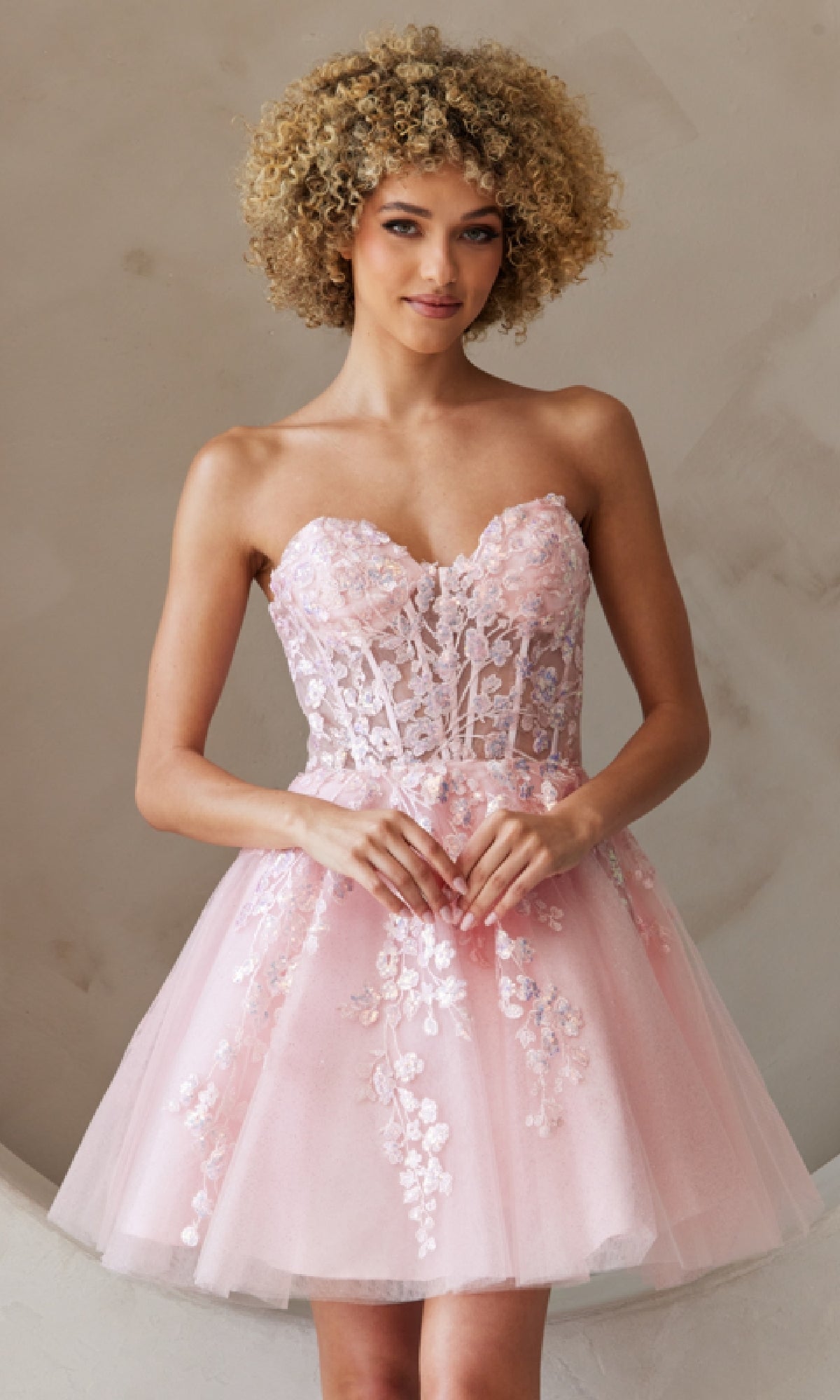 Wearing the Strapless Short Pastel Homecoming Dress BZ9024S by Amelia Couture, featuring floral lace details and a tulle skirt in pastel pink, this look pops beautifully against a neutral background.