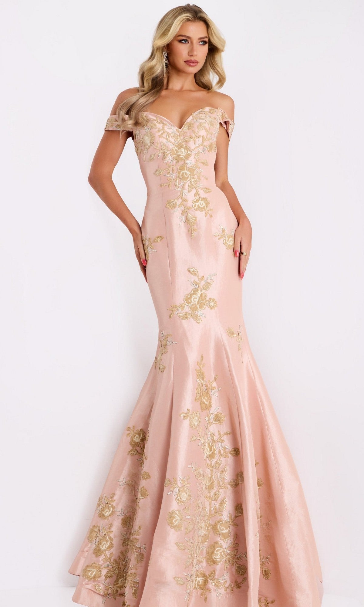 A woman poses elegantly against a plain white background in the Jovani Gold and Black Long Prom Dress 00635, an off-the-shoulder mermaid gown adorned with gold floral embroidery.