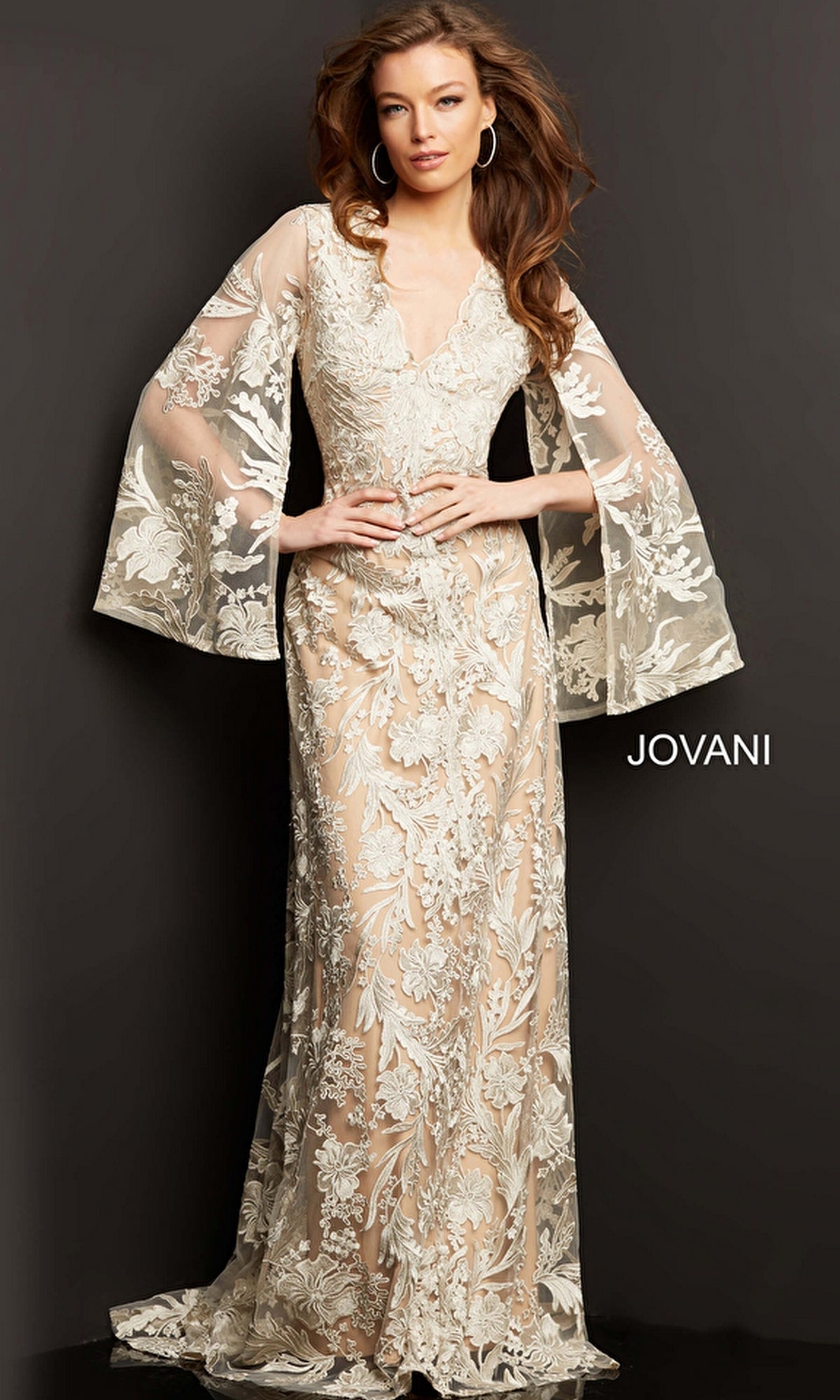 A woman poses against a dark background in the Embroidered Long Formal Gown 00752, featuring sheer cream-colored lace, wide long sleeves, and elegant floral embroidery throughout.