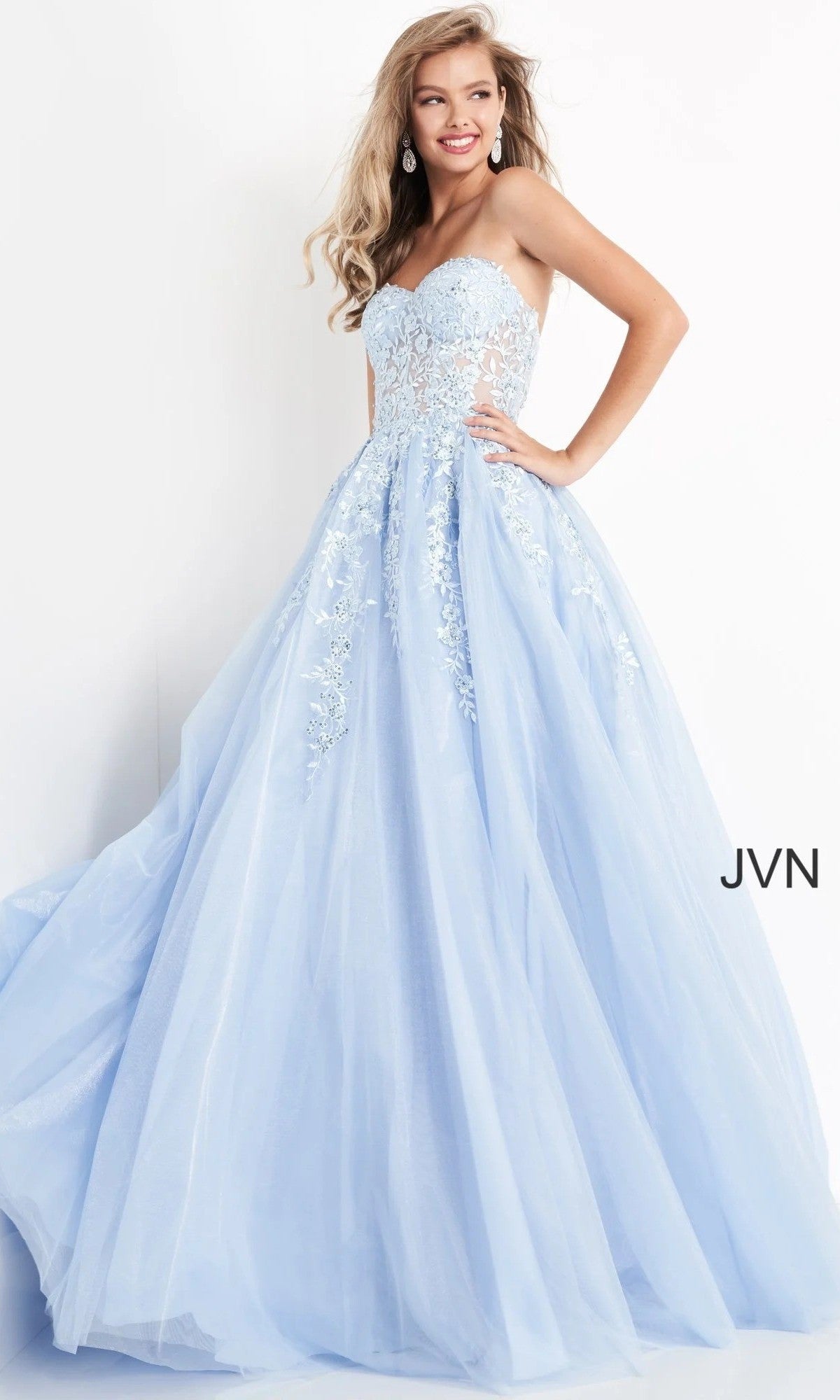 A woman poses and smiles against a white background wearing the Jovani 00915 Long Prom Dress in light blue, featuring a strapless lace-embroidered bodice and a flowing tulle ballgown skirt.