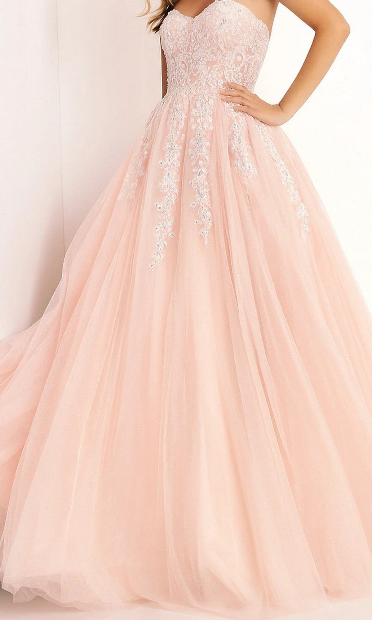 A woman wearing the Jovani 00915 long prom dress in blush, featuring a strapless lace-embroidered bodice with delicate white floral details and a tulle ballgown skirt.