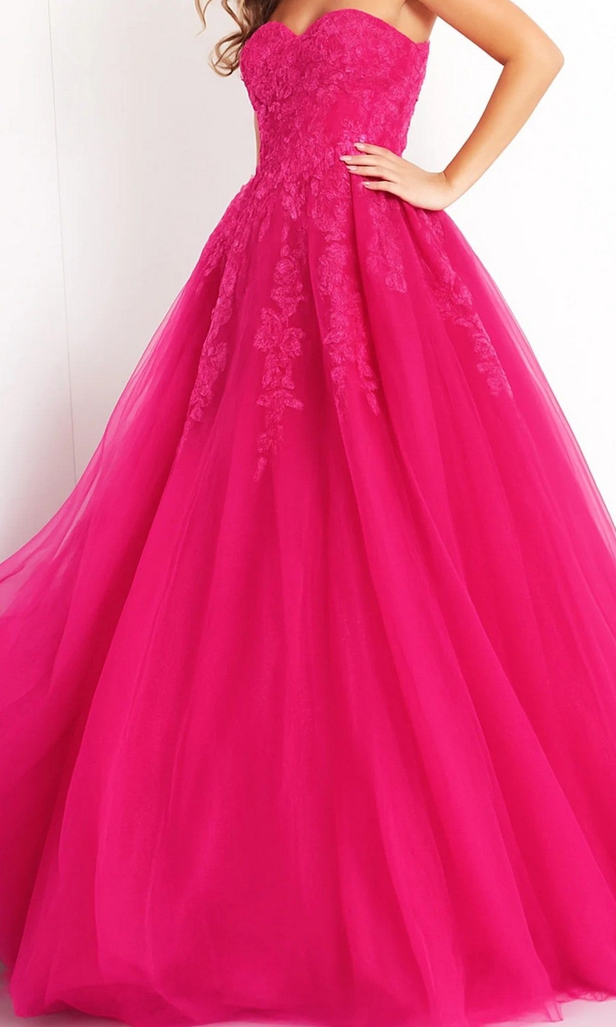 Woman wearing the Long Prom Dress: Jovani 00915—a hot pink strapless tulle ballgown with a fitted bodice and full skirt, adorned with exquisite floral lace details.