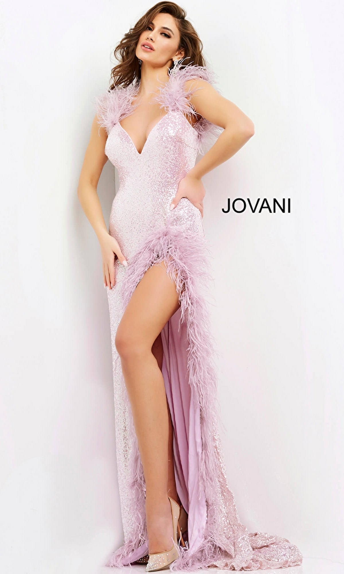 A woman wears the Long Prom Dress 06164 by Jovani, a light pink sequin formal gown with feather trim and a thigh-high slit, standing against a white background. The word