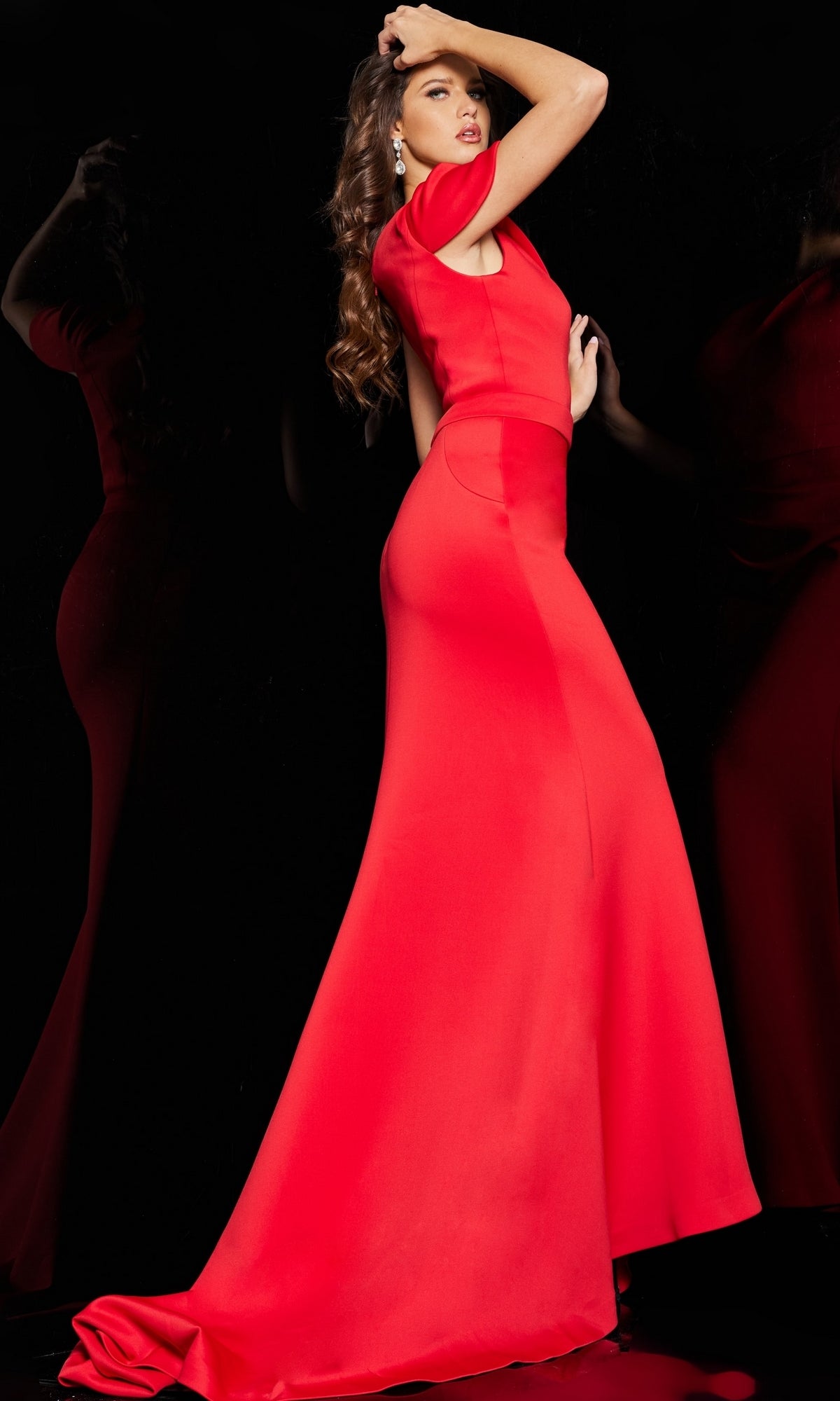A woman poses against a black background, wearing the Jovani 06753 long formal one-shoulder dress. Her hair is styled in loose waves and she raises one arm gracefully.