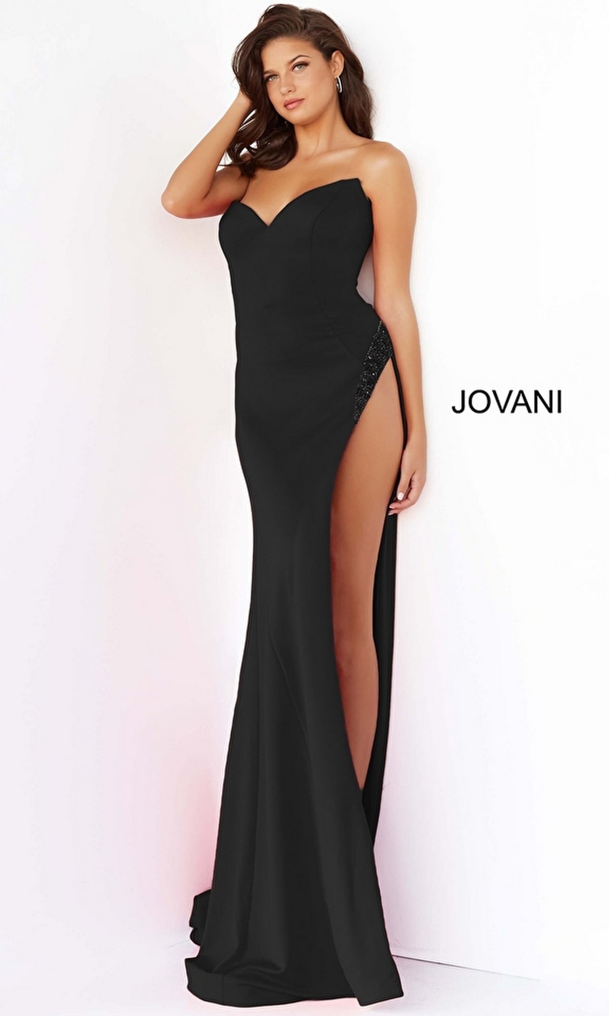 A woman poses in the Long Prom Dress 07138 by Jovani, a strapless formal gown with a sweetheart neckline and embellished high slit, set against a plain background featuring the