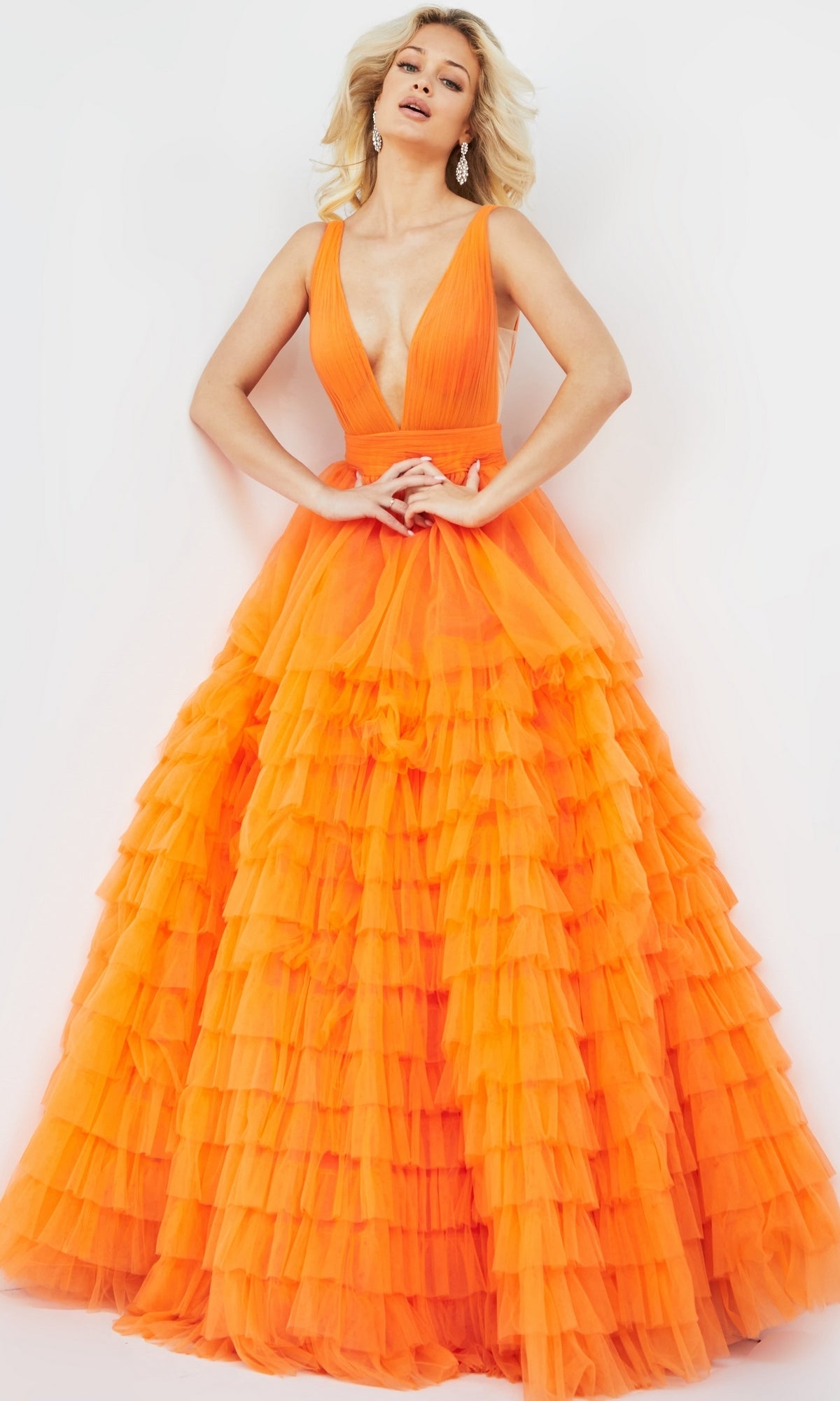 A woman poses against a white background in the Jovani V-Neck Long Ruffled Prom Ball Gown 07264, a sleeveless bright orange dress featuring a deep V-neck and layers of ruffled tulle.