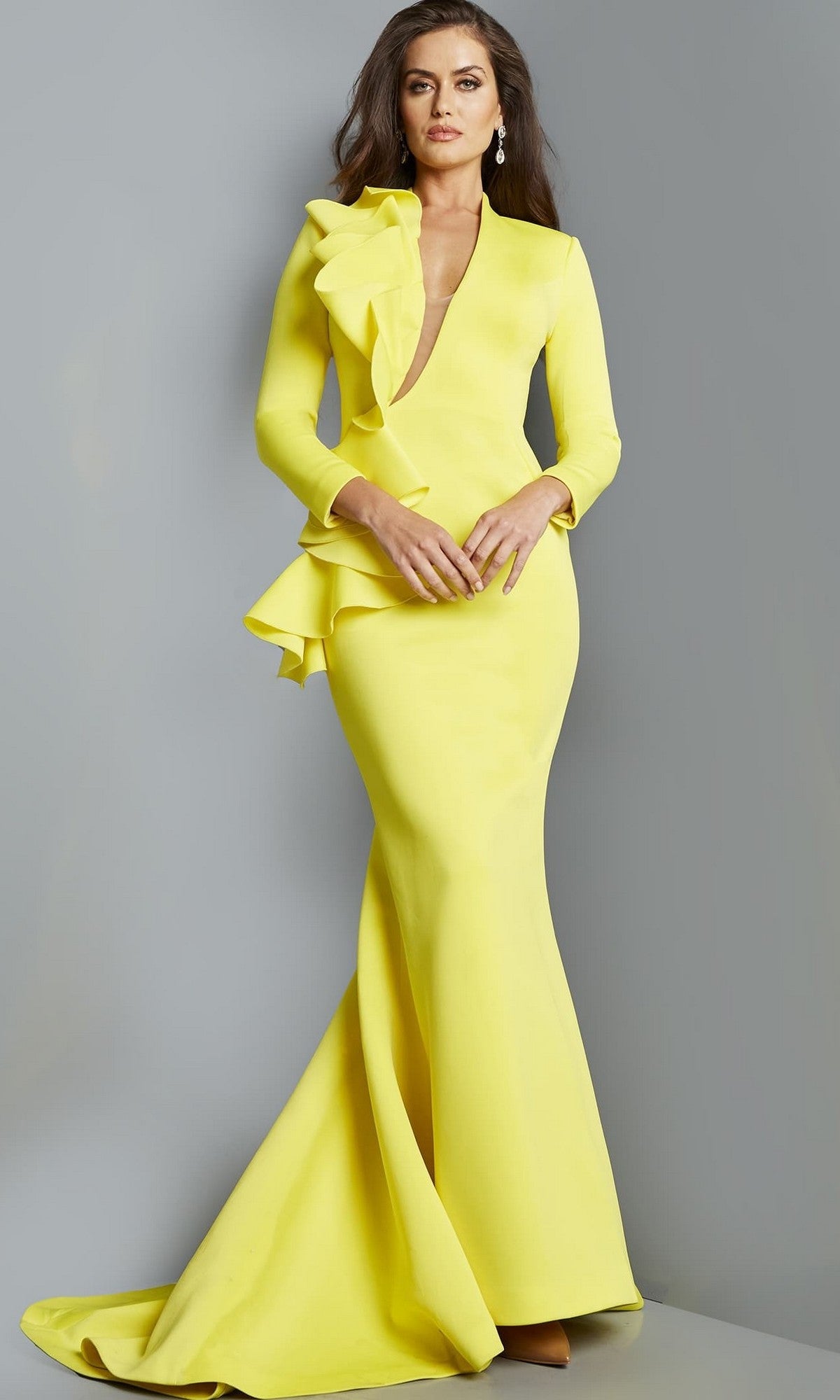 A woman wearing the Long Formal Dress: Jovani 07934, a bright yellow, form-fitting gown with ruffle details, stands against a plain gray background.