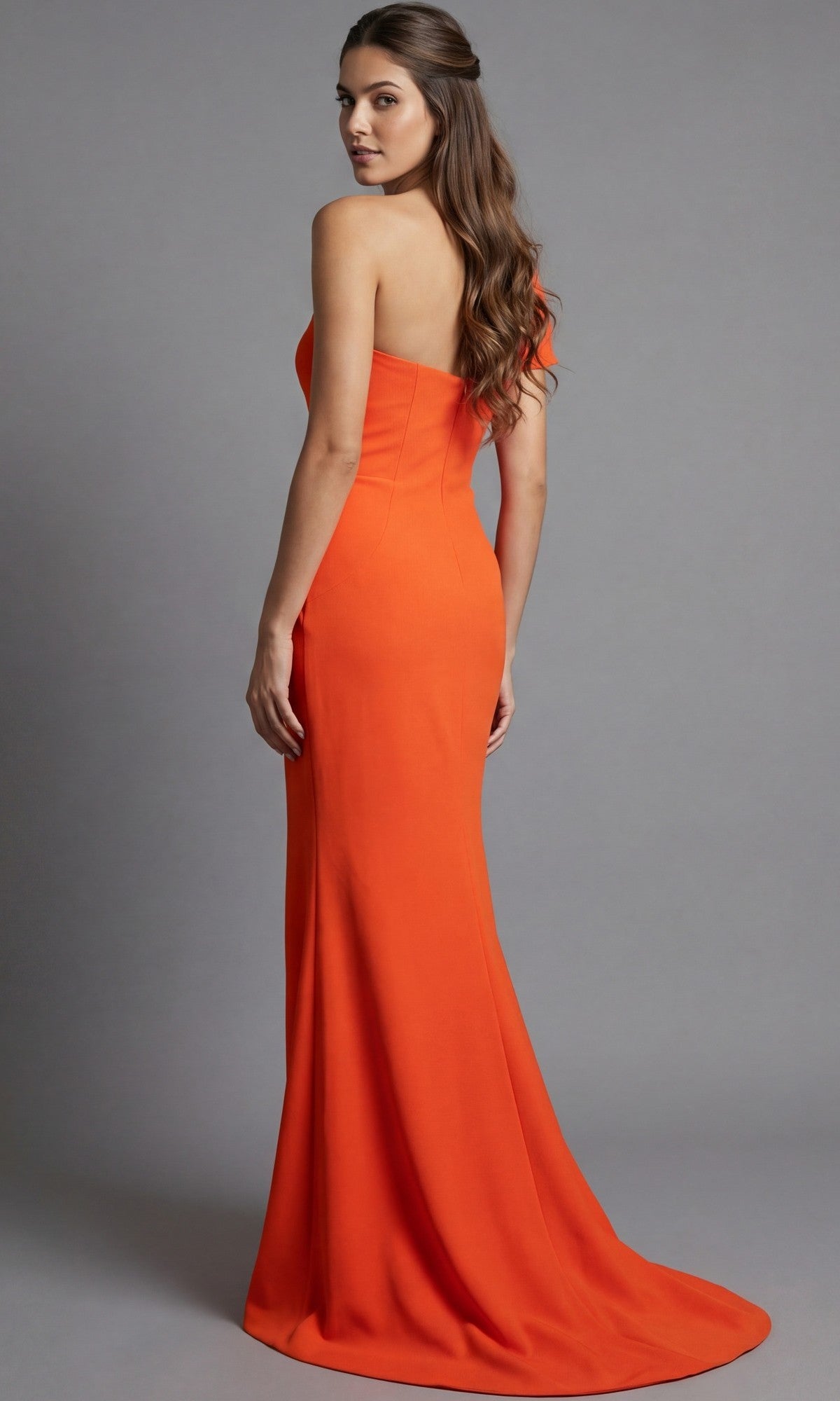 A woman wearing the Long Formal Dress: Jovani 09961—a floor-length, strapless orange gown—stands against a plain gray background, facing away while looking over her shoulder.