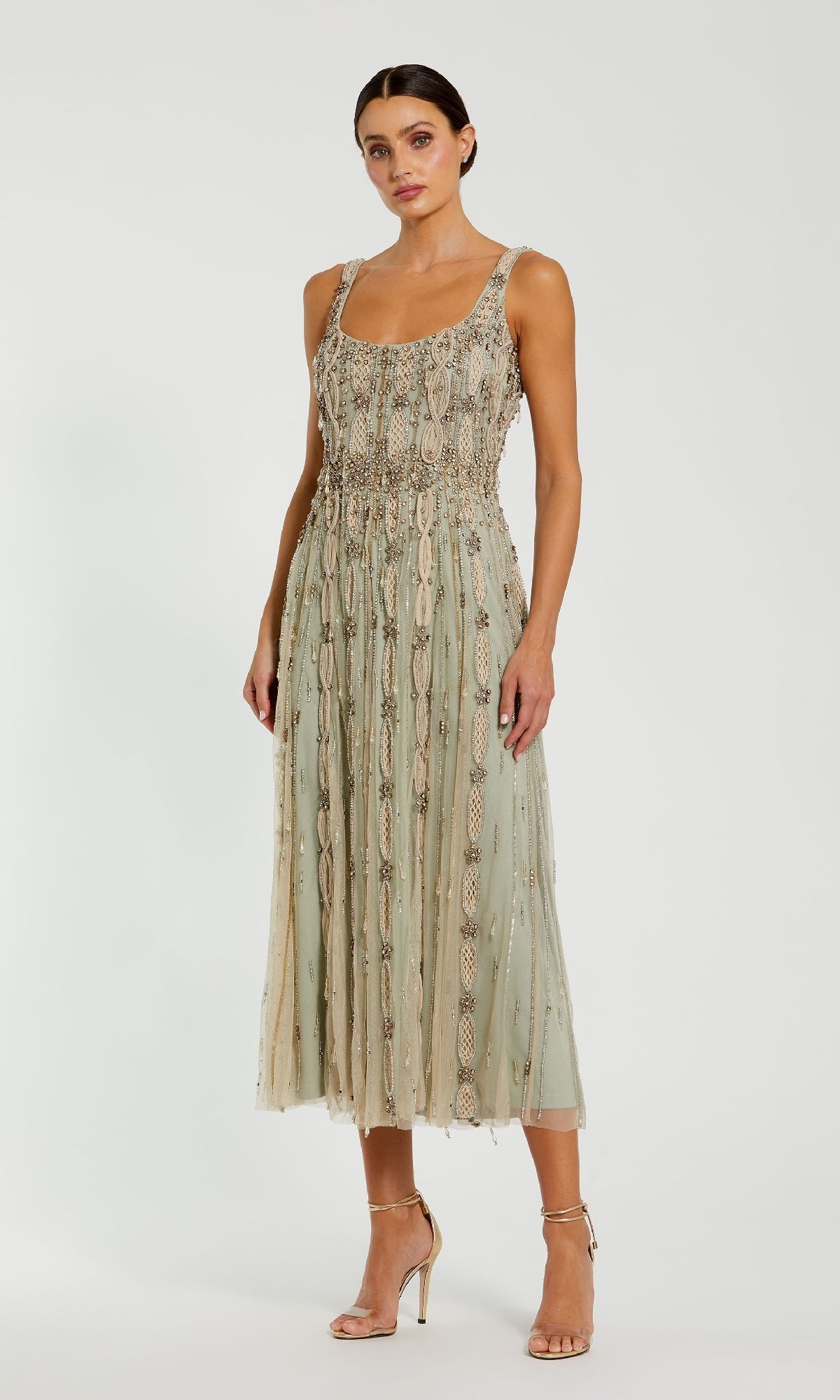 A woman wears the Mac Duggal 10078 Beaded Midi Wedding Guest Dress in sage green with intricate beading and embroidery, paired with strappy high-heeled sandals, standing against a plain white background.