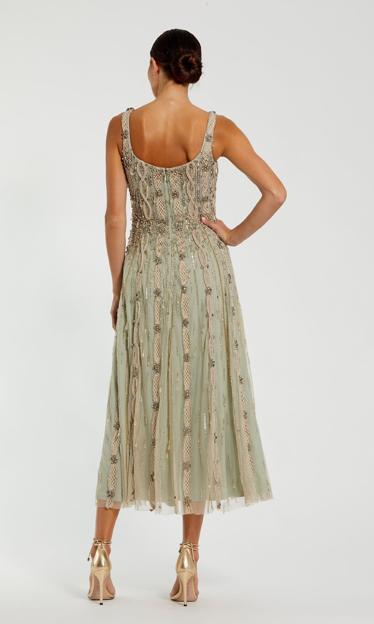 A woman faces away, wearing the Beaded Midi Wedding Guest Dress: Mac Duggal 10078 in sage green with a flared skirt, paired with gold high-heeled sandals.