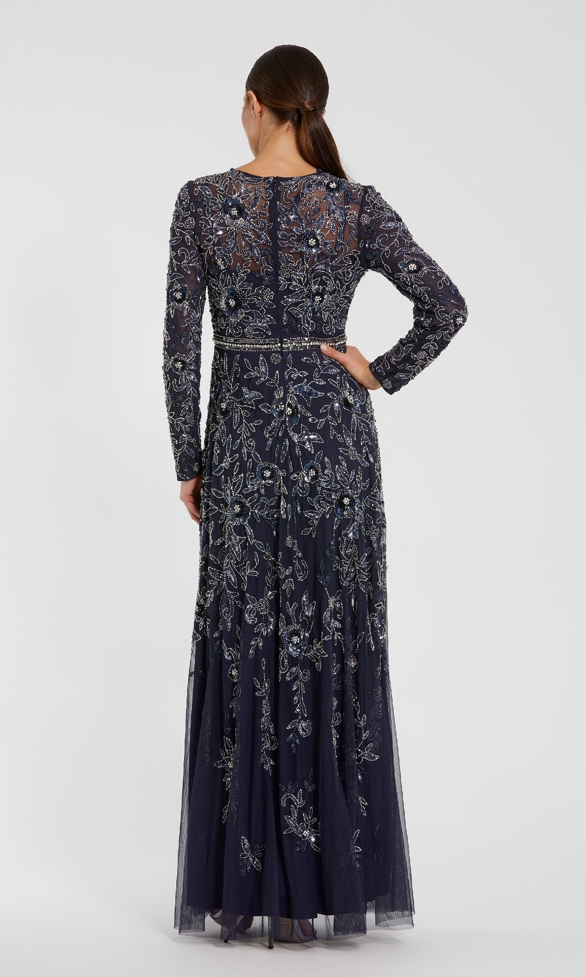 A woman faces away, wearing the Mac Duggal 10093 Long Sleeve Beaded Formal Dress featuring intricate silver and blue floral embroidery.