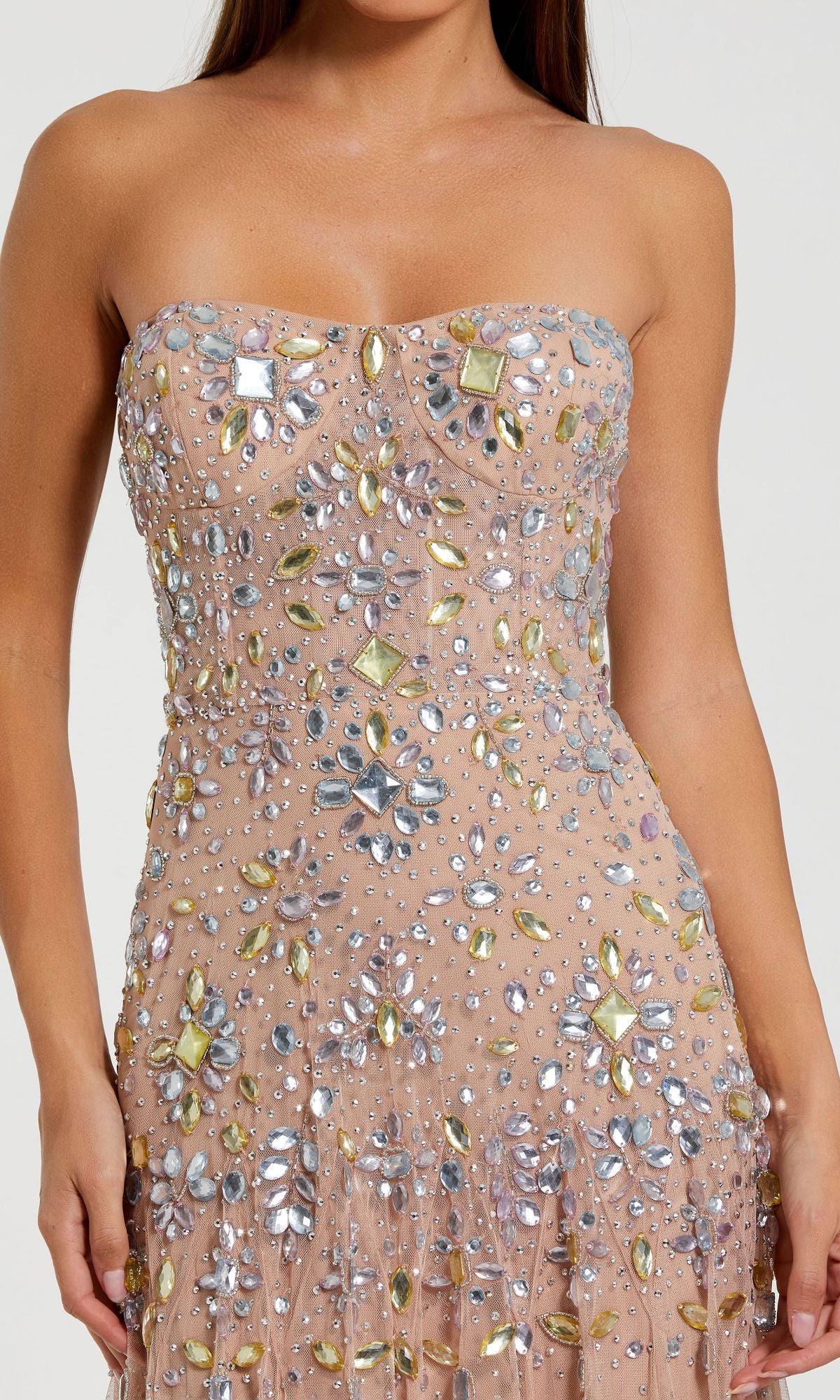 A woman wearing the Strapless Light Pink Prom Gown, Mac Duggal 10100, featuring a long silhouette with large silver and gold gem floral embellishments.