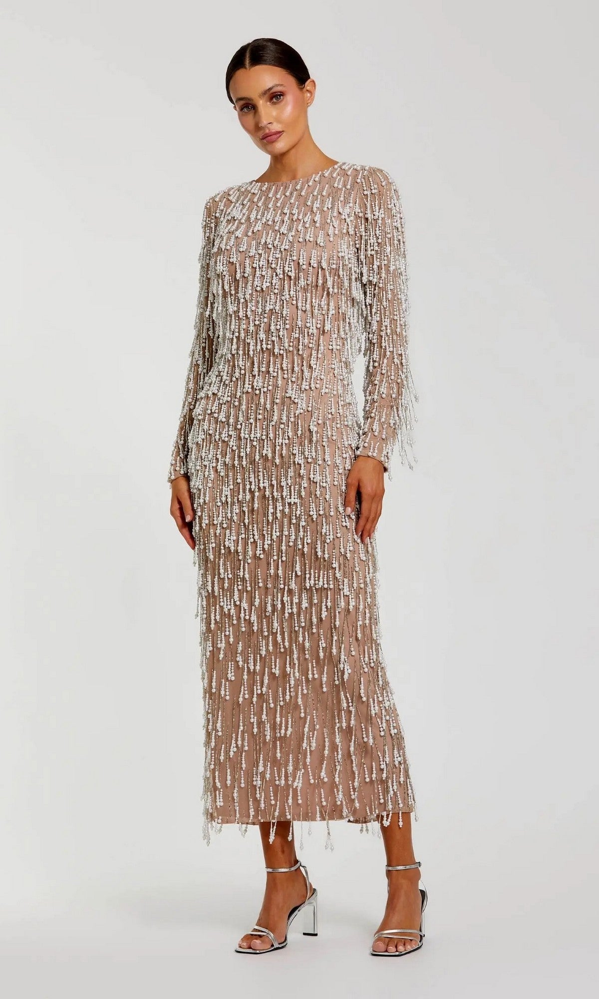 A woman wears the Midi Wedding Guest Dress: Mac Duggal 10120 in Ivory Nude, featuring long sleeves with silver sequin and pearl-beaded fringe, paired with metallic block-heel sandals against a plain background.