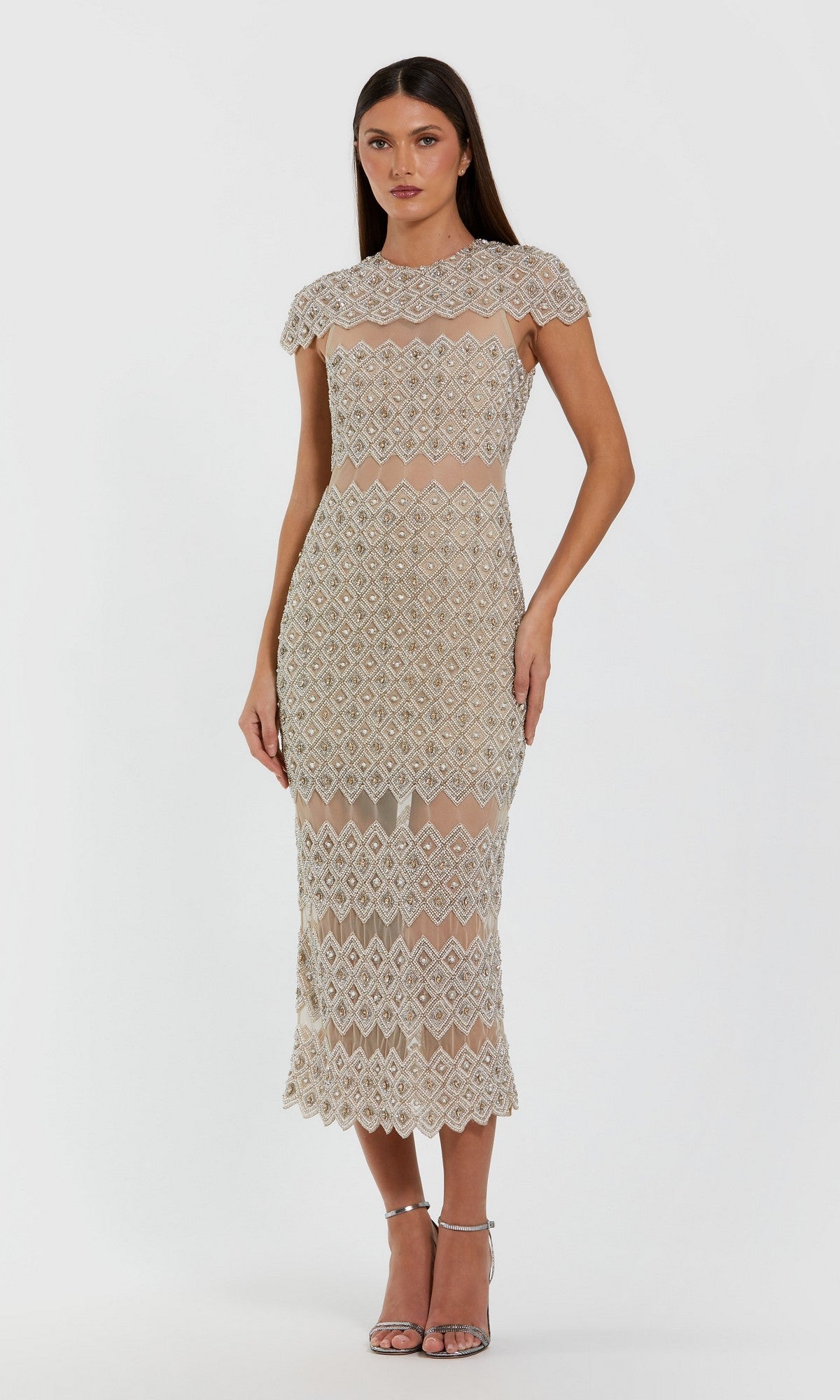 A woman wearing the Long Formal Dress: Mac Duggal 10147 in Ivory Nude, a fitted sheath dress with diamond-shaped geometric beadwork and short sleeves, paired with open-toe heels, stands against a plain white background.