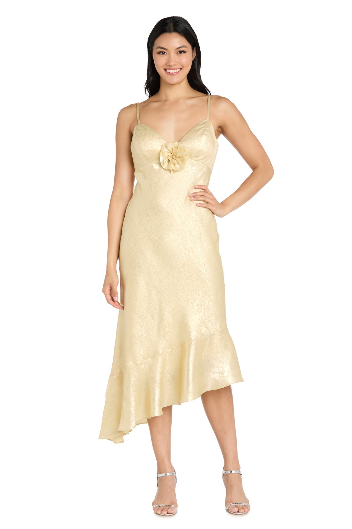 A woman smiles in strappy heels, wearing the Shimmer Midi Semi-Formal Dress: Morgan 10251—a light gold, sleeveless dress with thin straps, flower detail at the bust, and asymmetrical hem—perfect for parties or semi-formal events.