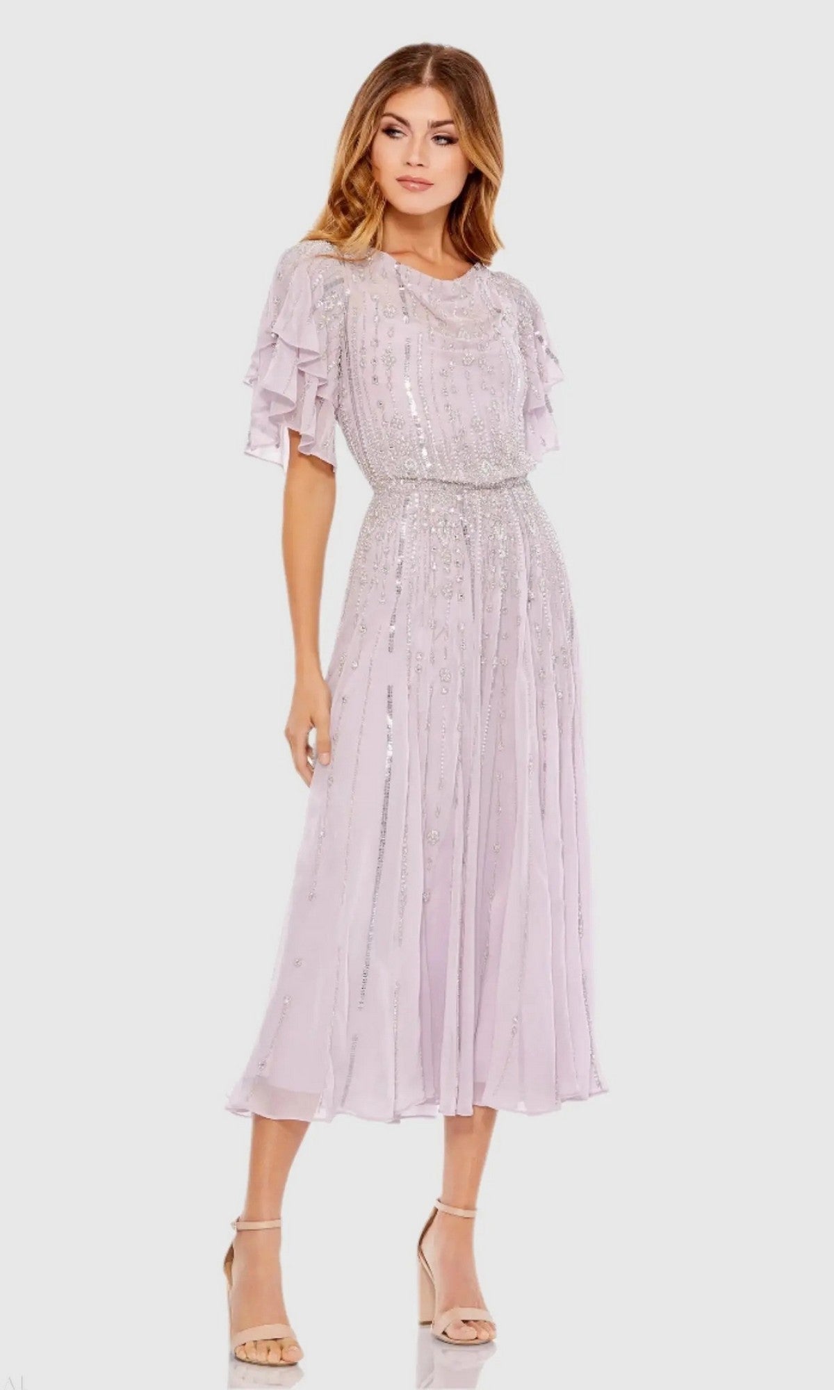 A woman wearing the Mac Duggal 10690 lilac midi wedding guest dress with short ruffled sleeves and silver heels stands against a plain light background.