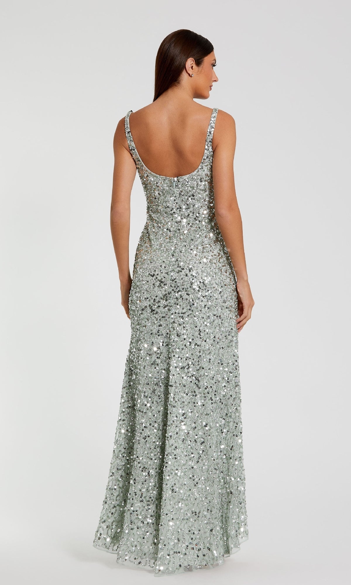 A woman faces away, wearing the Mac Duggal 10705 Sparkly Long Sequin Formal Dress with a fitted silhouette and dramatic low back, set against a plain light background.