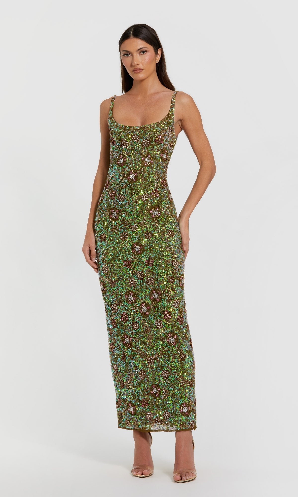 A woman wears a Mac Duggal 10755 Sequin Formal Dress with Back Slit, sleeveless and floor-length in green with beaded floral print, paired with nude heels, standing against a plain white background.