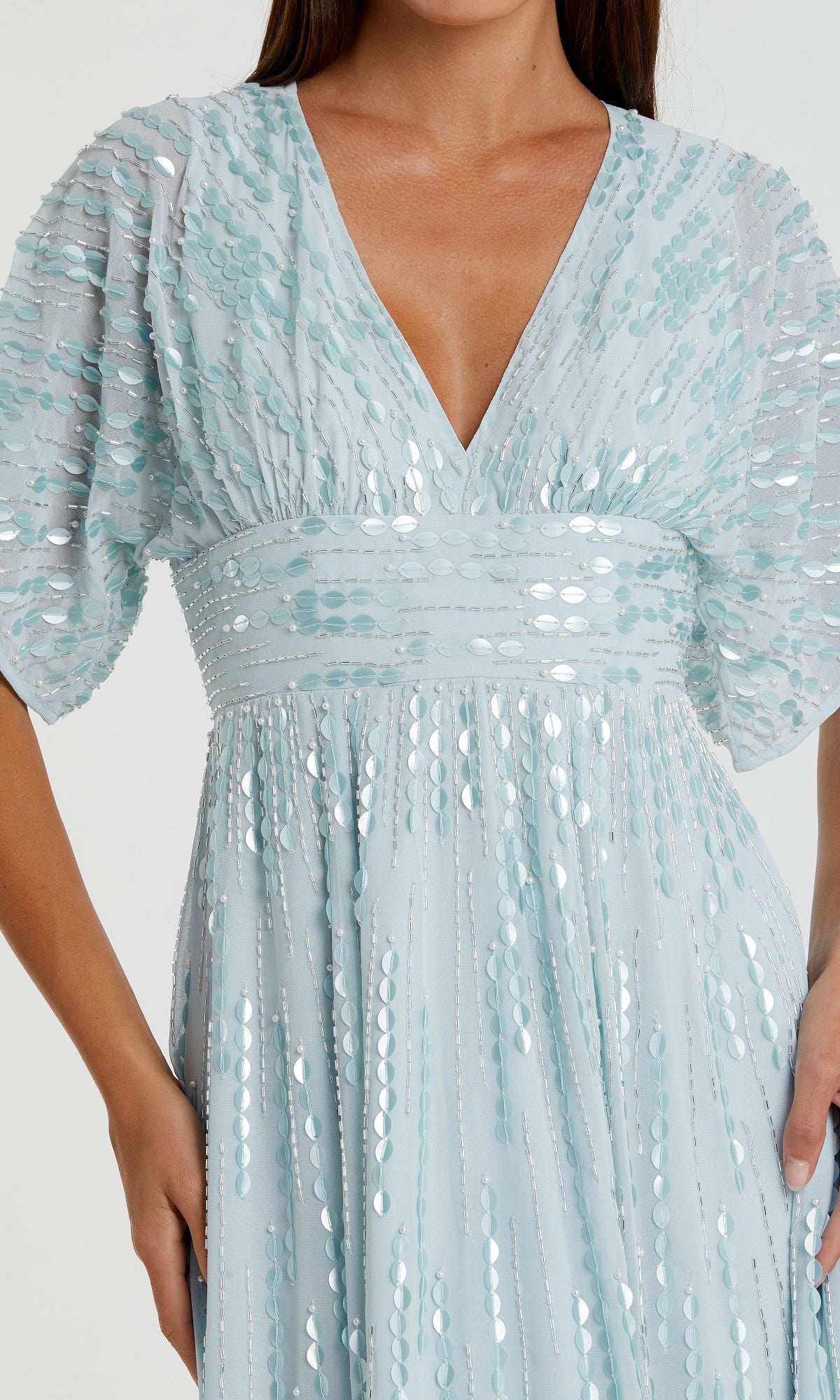 A woman wears the Mac Duggal 10807, a powder blue formal dress featuring short puff sleeves, a deep V-neckline, and shimmering sequins—an elegant choice for special occasions.