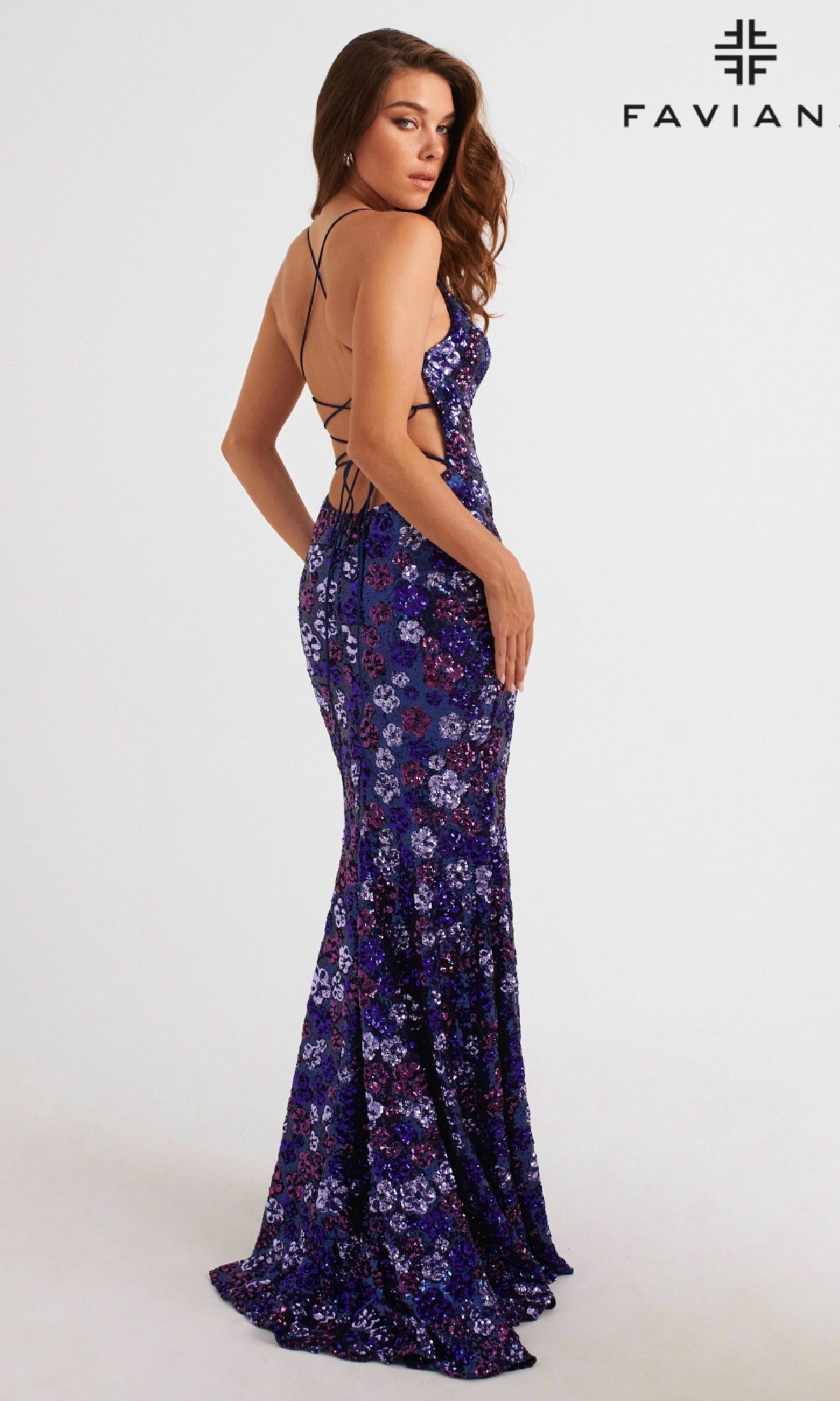 A woman in the Faviana Floral-Sequin Long Prom Dress 11000, a floor-length dark blue gown with sparkling sequins and a strappy open back, stands sideways. The brand name
