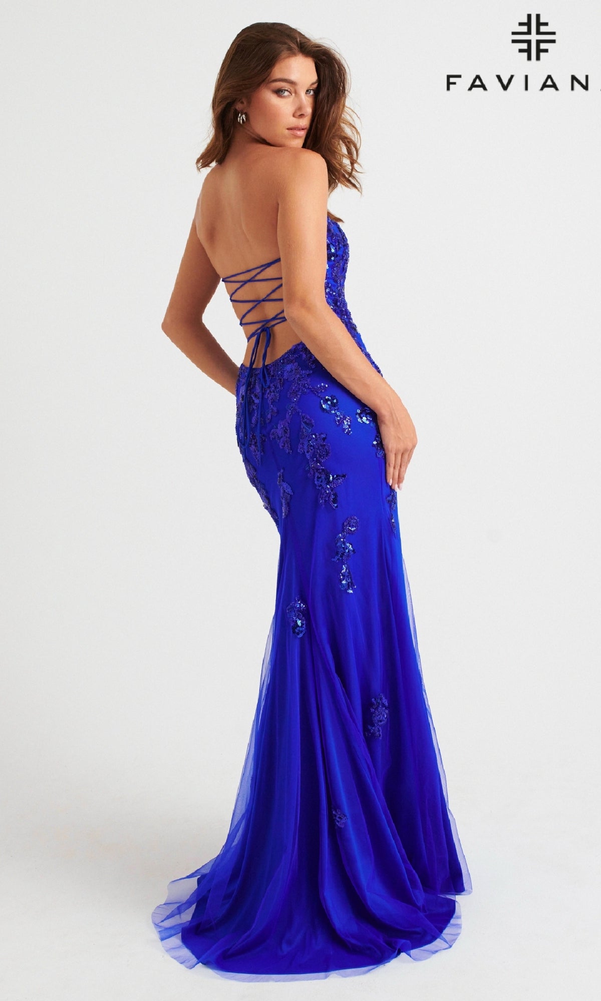 A woman faces away from the camera in the Faviana Strapless Long Beaded Prom Dress 11004, a royal blue, floor-length designer gown with floral embellishments, a fitted silhouette, lace-up back, and beaded details.