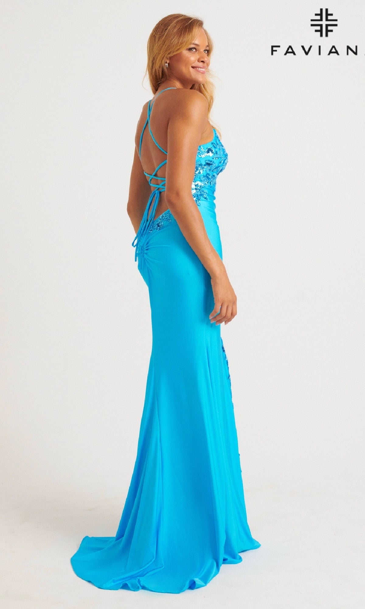 A woman models the Faviana Tonal-Embroidered Long Prom Dress 11017, a fitted blue gown with sequin details and crisscross back straps, standing before a plain white background with the FAVIANA logo.