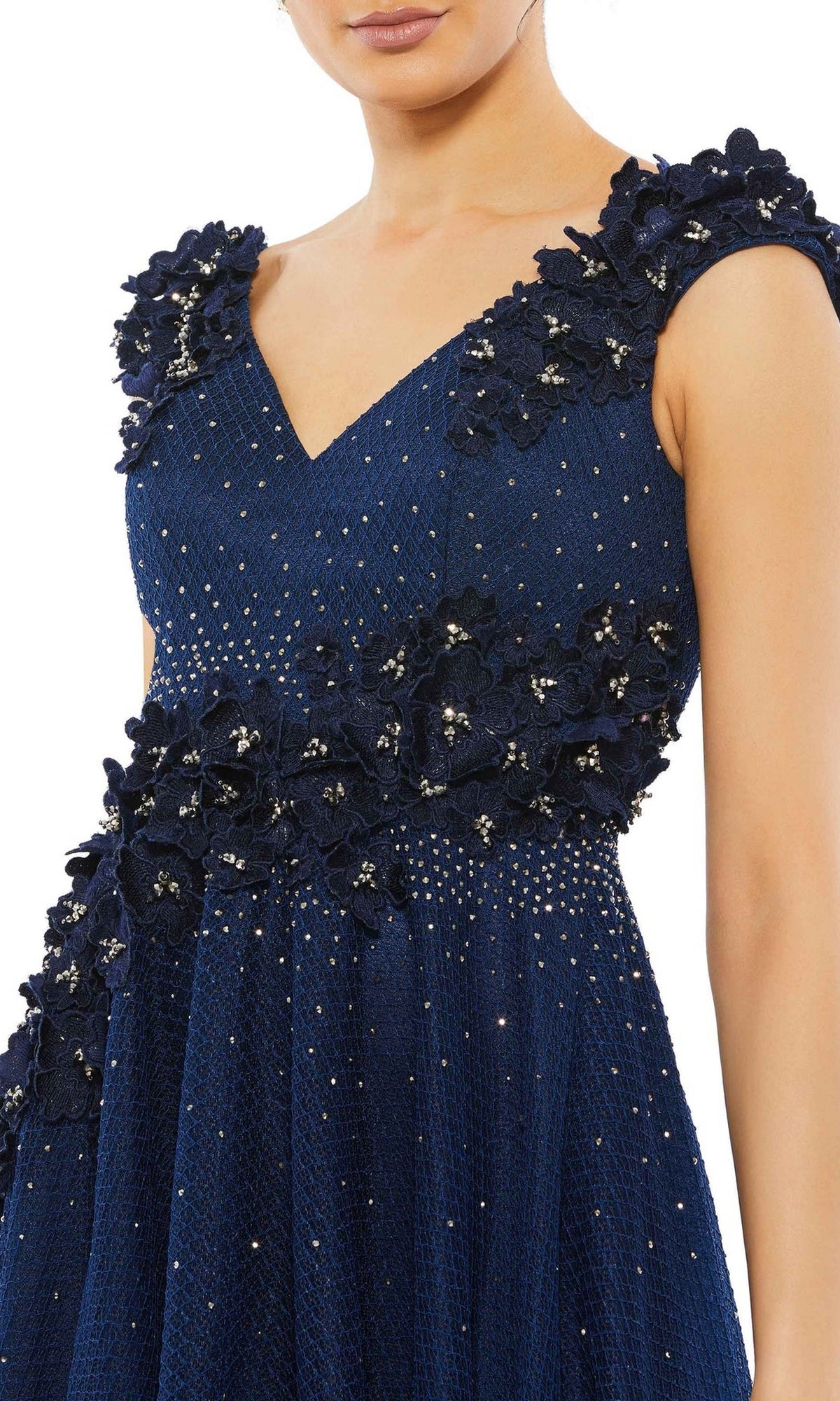 A woman wears the Mac Duggal V-Neck Midnight Blue Formal Dress 11152, an A-line gown with embroidered floral appliques and sparkling embellishments on textured fabric.