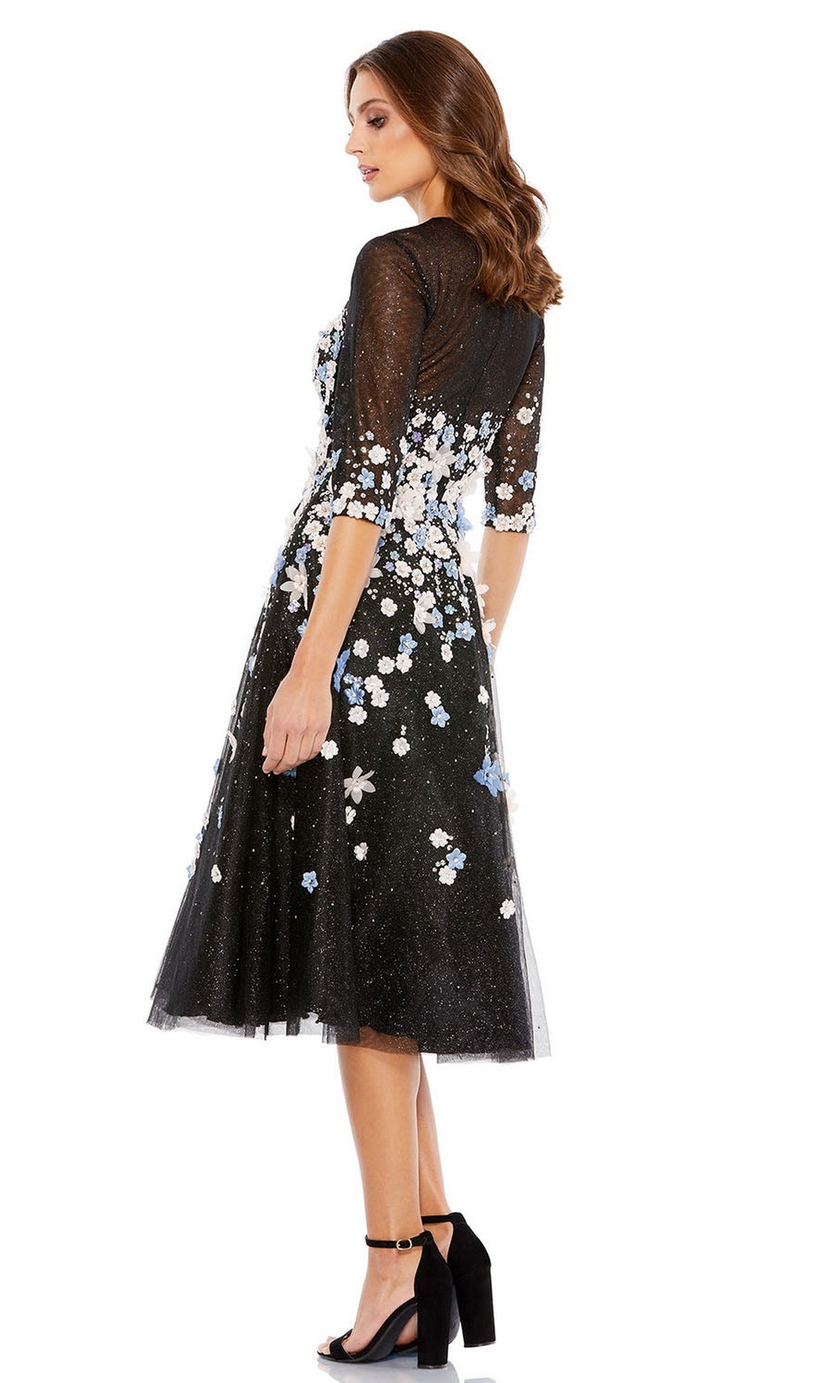 A woman in profile wears the Short Wedding Guest Dress 11161 by Mac Duggal—an elegant, black floral embroidered knee-length dress with sheer sleeves, styled with black high-heeled sandals, perfect for semi-formal occasions.