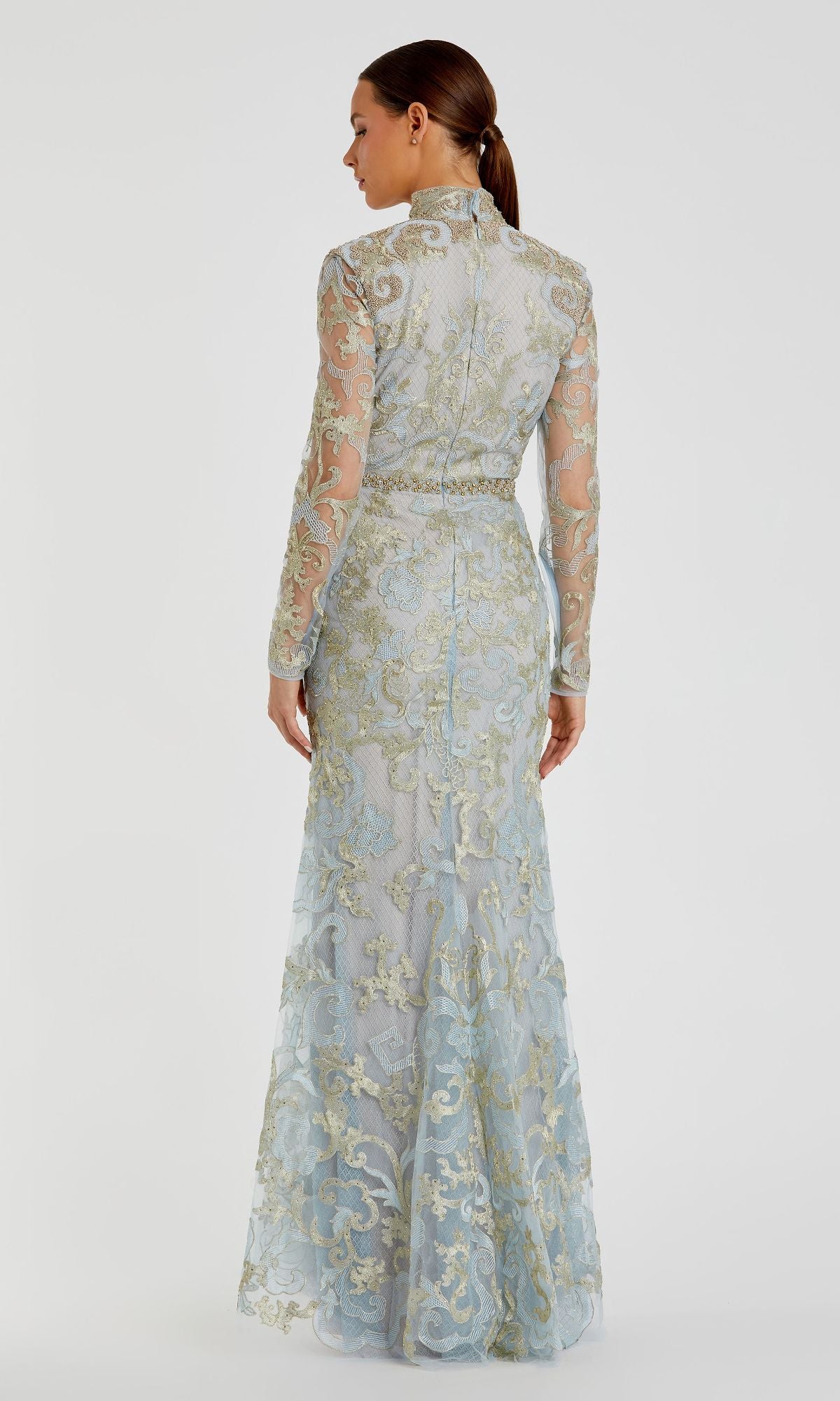A woman is shown from the back wearing the Mac Duggal 11165 Long Sleeve Lace Formal Gown, a vintage-style evening dress with a high neck and intricate gold and blue lace embroidery.