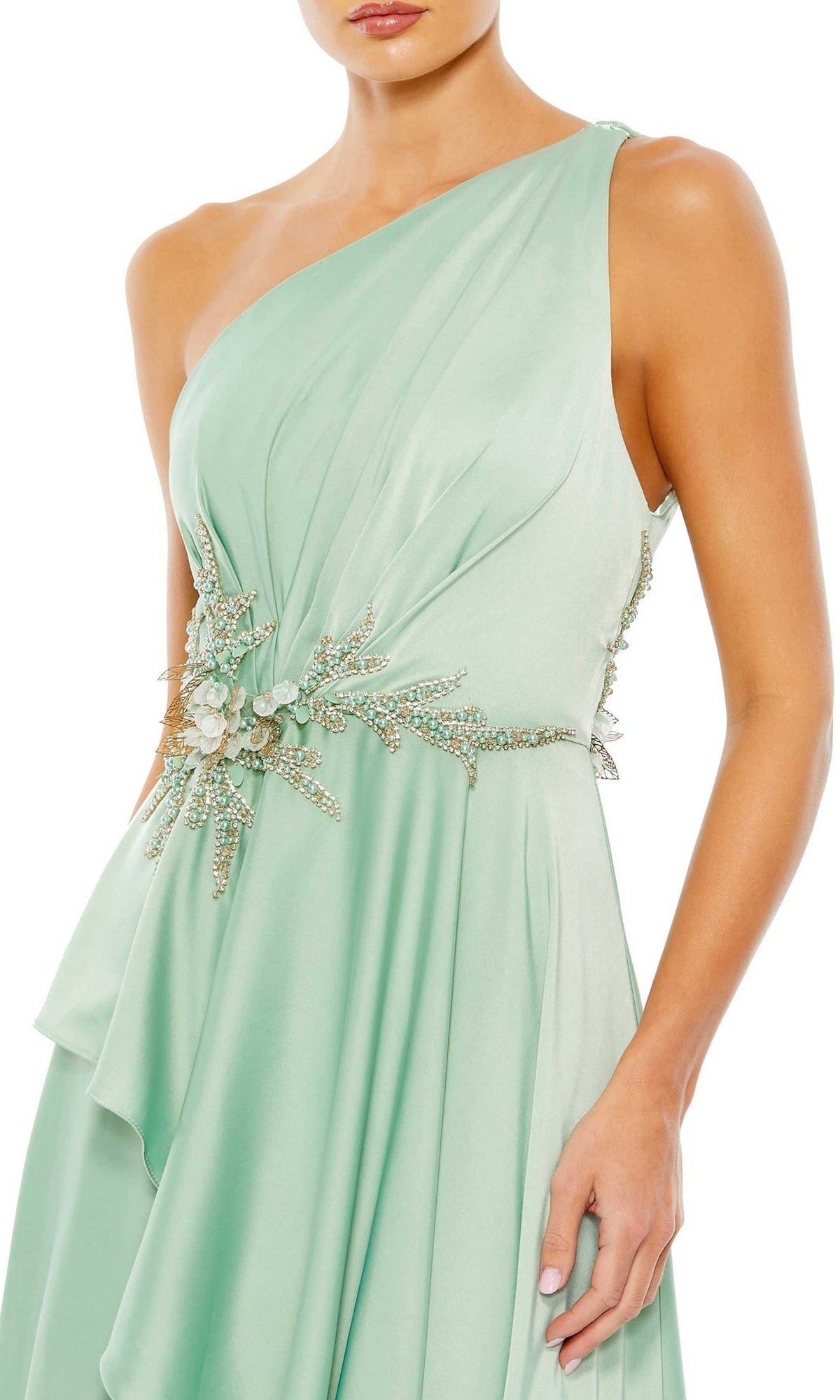 A woman wearing the Long Formal Dress 11262 by Mac Duggal—a light green, one-shoulder gown with an embellished waist, jeweled floral details, and a draped, flowing skirt.