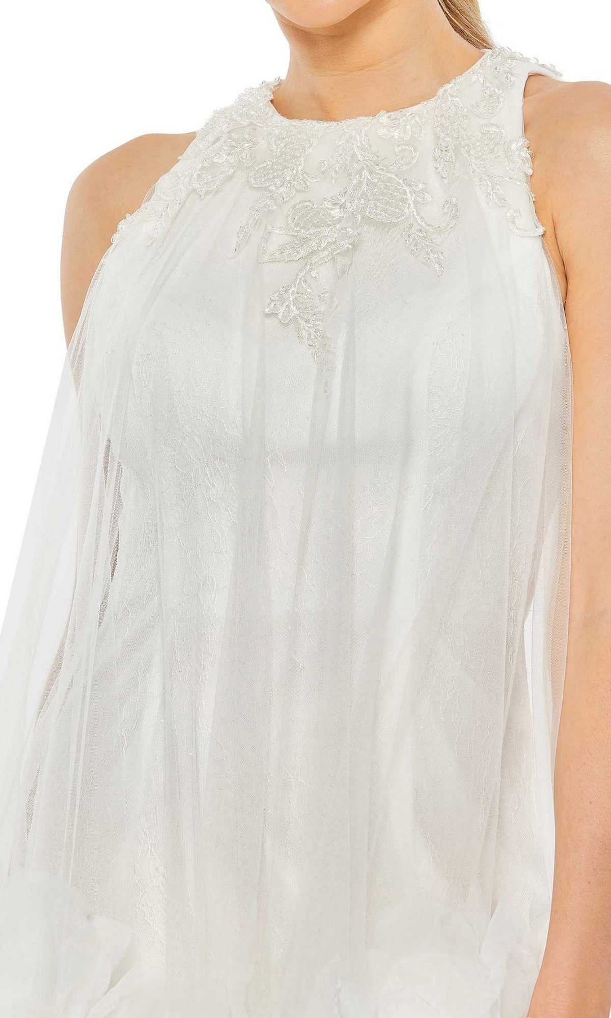 A woman wears the Short Homecoming Dress 11294 by Mac Duggal, a sleeveless white gown with lace beaded neckline embellishments and a sheer fabric overlay.
