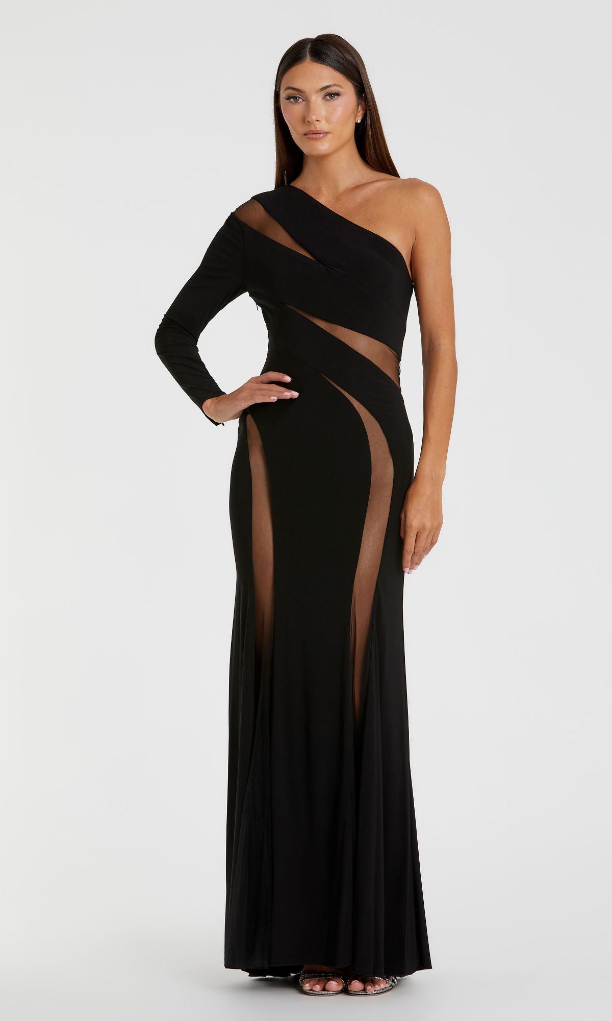 A woman models the Cut-Out Long Black Formal Dress: Mac Duggal 11311, featuring sheer mesh cutouts and a single long sleeve, while posing gracefully against a plain white background.