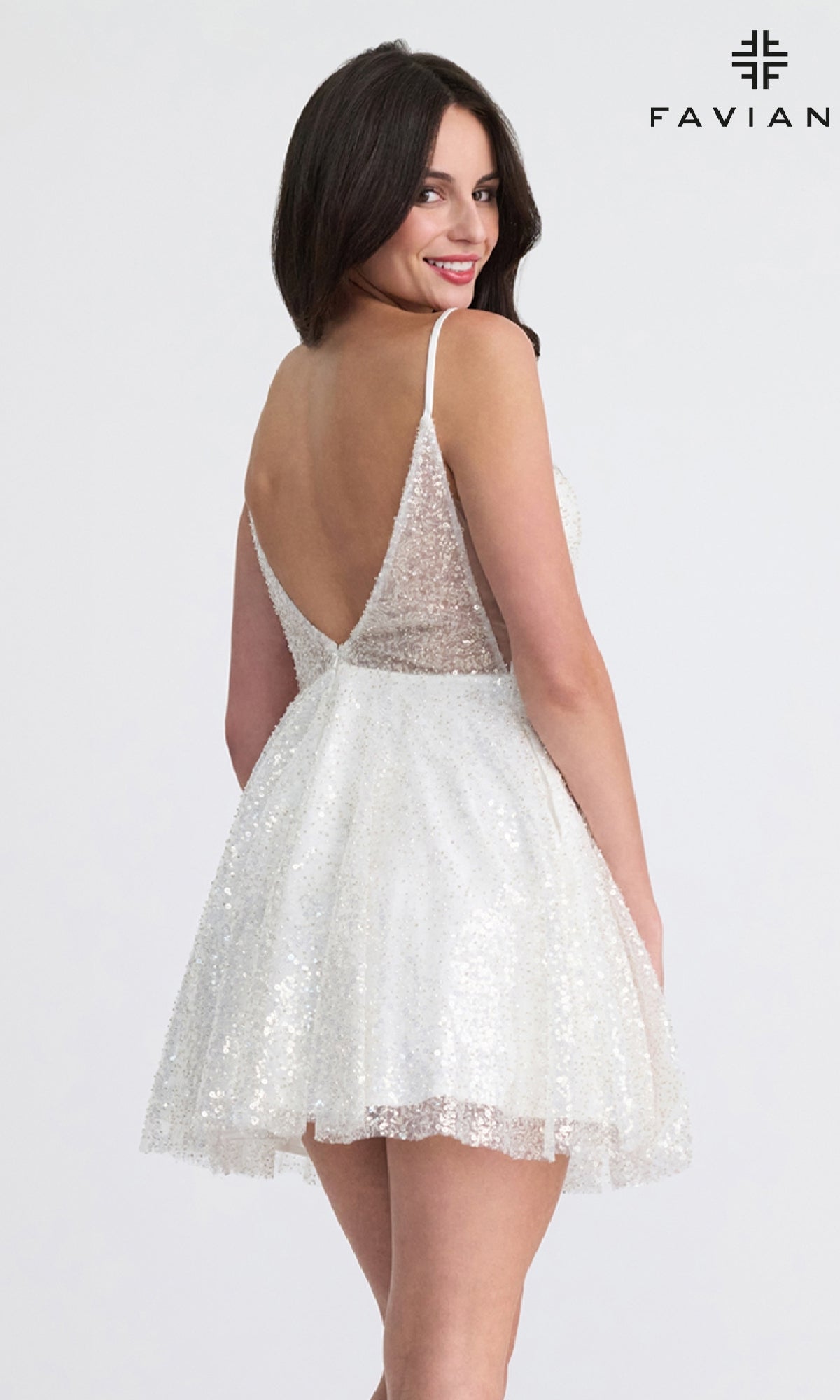 A woman poses against a plain background in the Faviana 11319, a short A-line sequin hoco dress in white with an elegant deep V back. The brand name