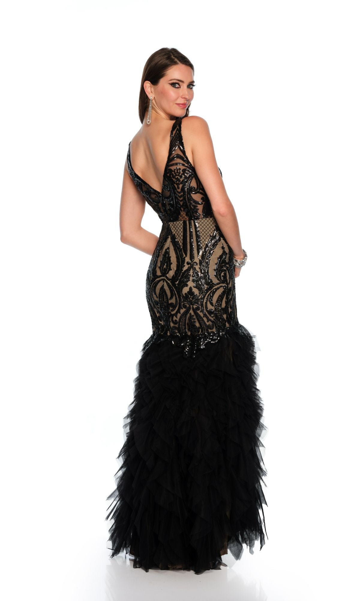 Woman poses with her back slightly turned against a white background, wearing the Long Formal Dress 11325 by Dave and Johnny—a sleeveless, form-fitting black lace and tulle mermaid gown with a v-neckline.
