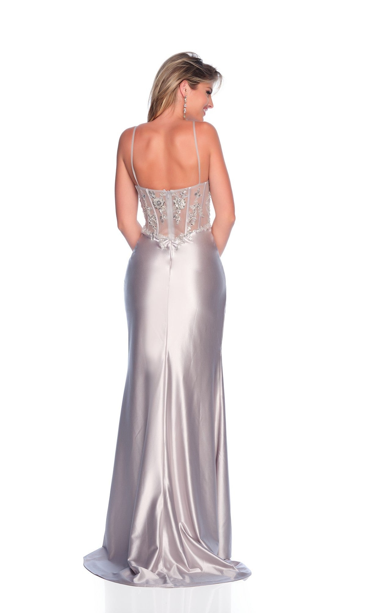 A woman stands with her back to the camera in the Sheer-Bodice Long Prom Dress by Dave & Johnny 11330, featuring a satin silver finish, thin straps, and an embellished sheer back panel.