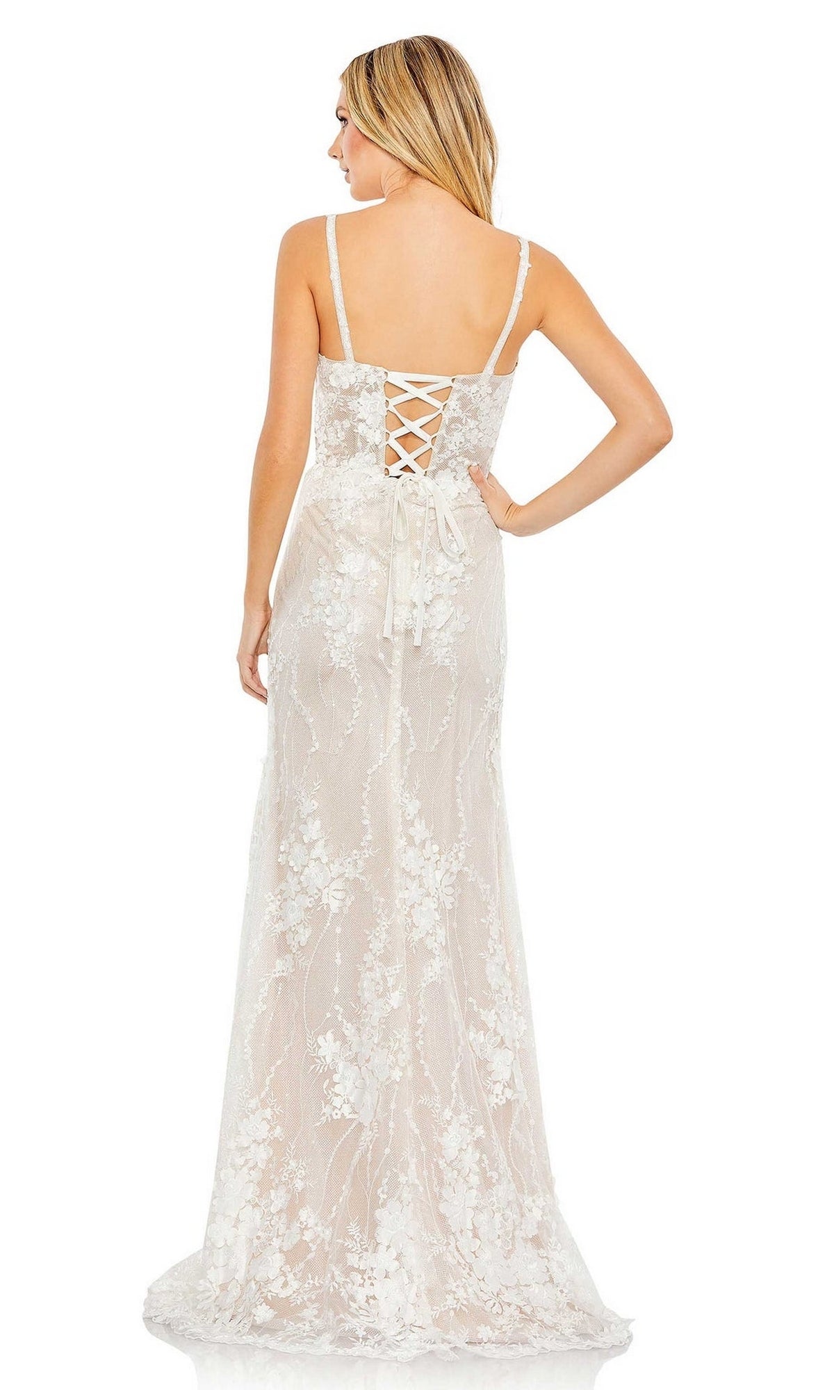 A woman stands with her back to the camera in the Long Formal Dress 11331 by Mac Duggal, a sleeveless, floor-length white lace embroidered gown featuring floral patterns and a lace-up back.