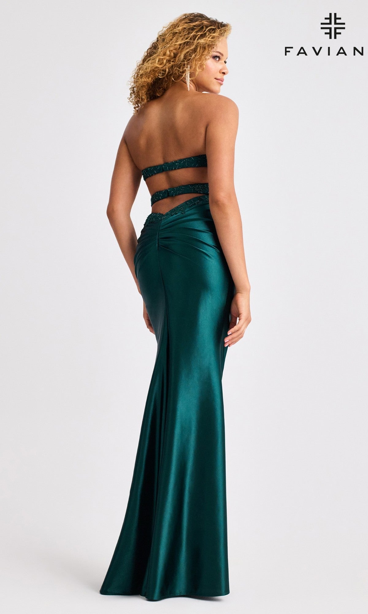 A woman models the Faviana 11429 long prom dress—a fitted, strapless satin gown in dark green with back cutouts and ruching—facing away from the camera. The Faviana logo appears in the top right corner.