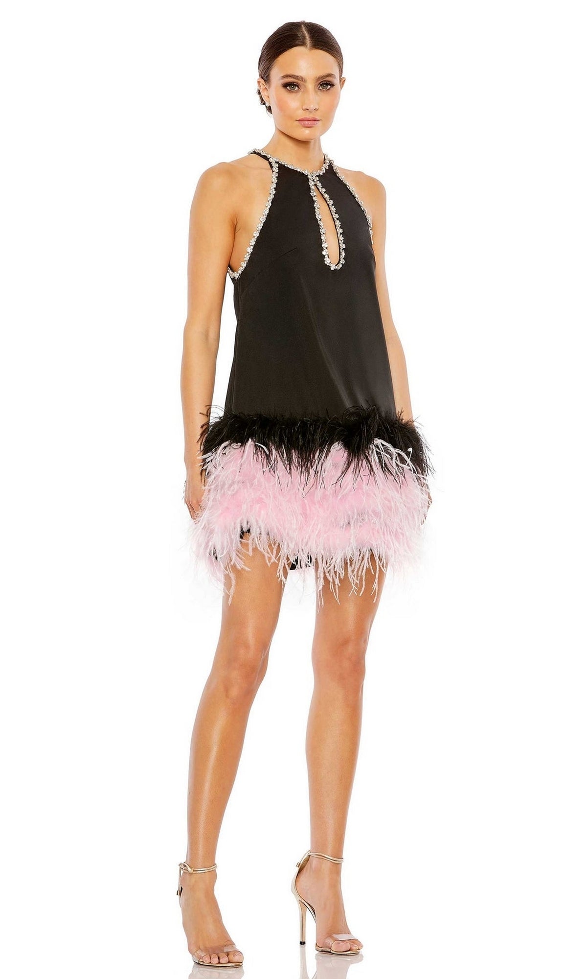 A woman wears the Short Homecoming Dress 11437 by Mac Duggal—sleeveless with a black feather trim, keyhole neckline, and black and pink accents—paired elegantly with silver high-heeled sandals.