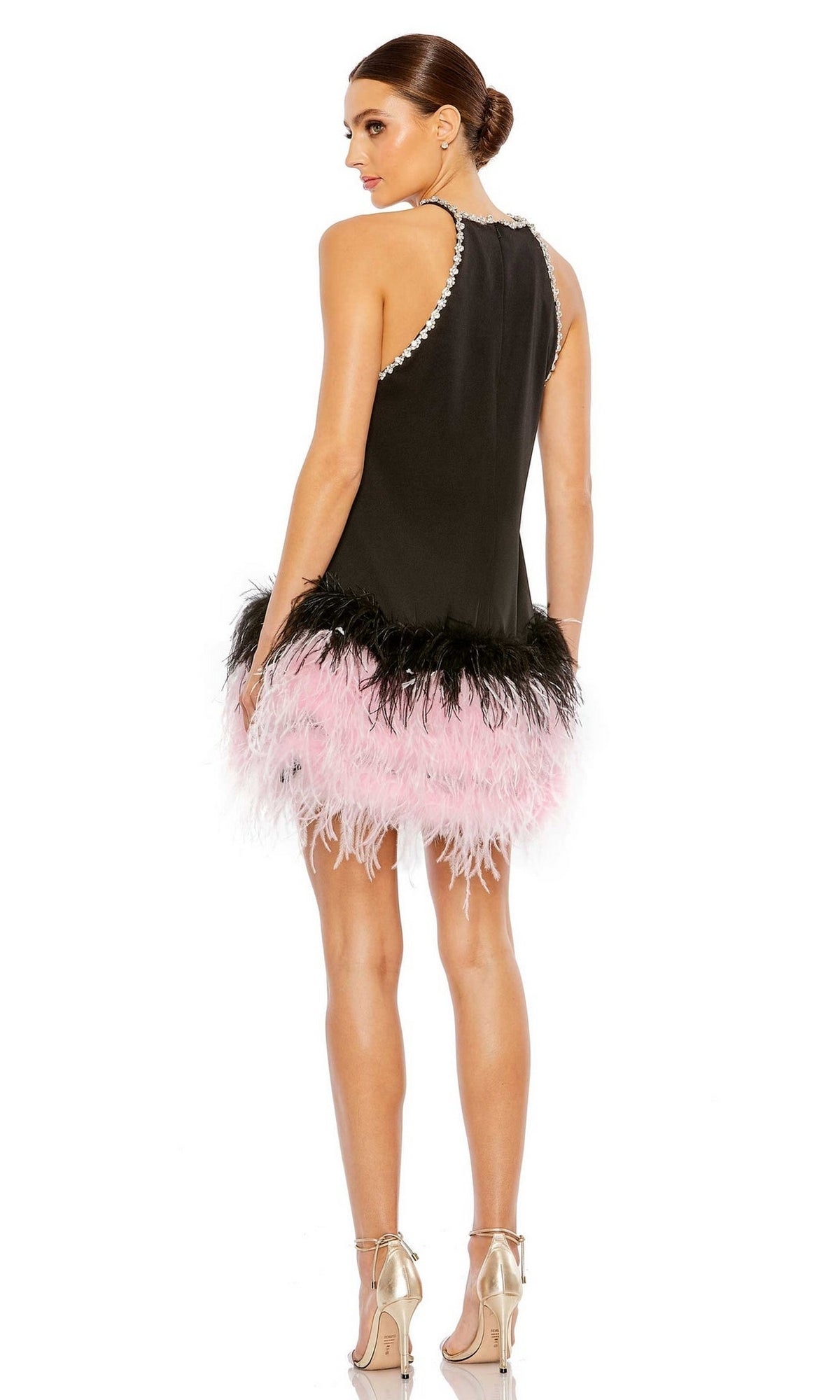 A woman faces away wearing the Mac Duggal Short Homecoming Dress 11437—a sleeveless black dress with pearl accents and a pink and black feathered hem—paired with silver high-heeled sandals.