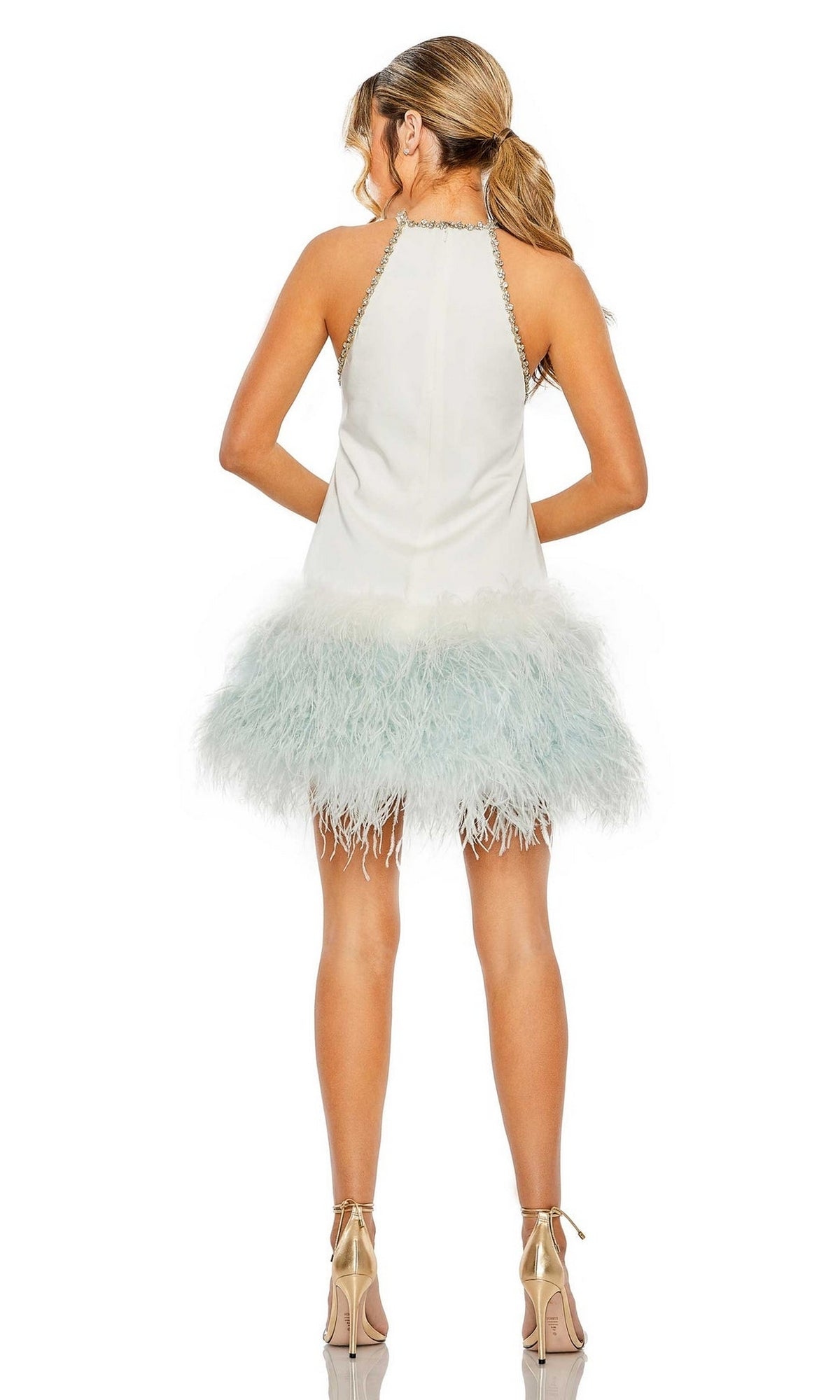 A woman faces away, her hair in a ponytail, wearing the Short Homecoming Dress 11437 by Mac Duggal—a sleeveless dress with a white feathered skirt and metallic high heels.