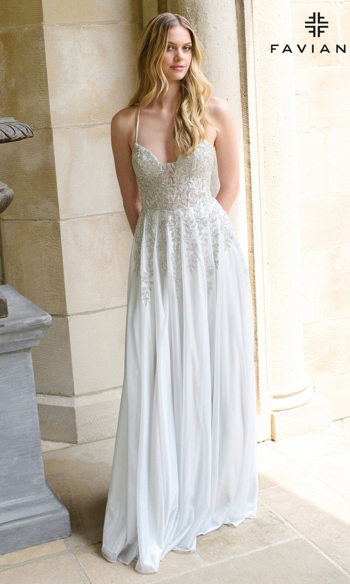A woman poses by a stone column in the Faviana 11449 long prom dress, featuring a light, sleeveless A-line silhouette and lace bodice details.