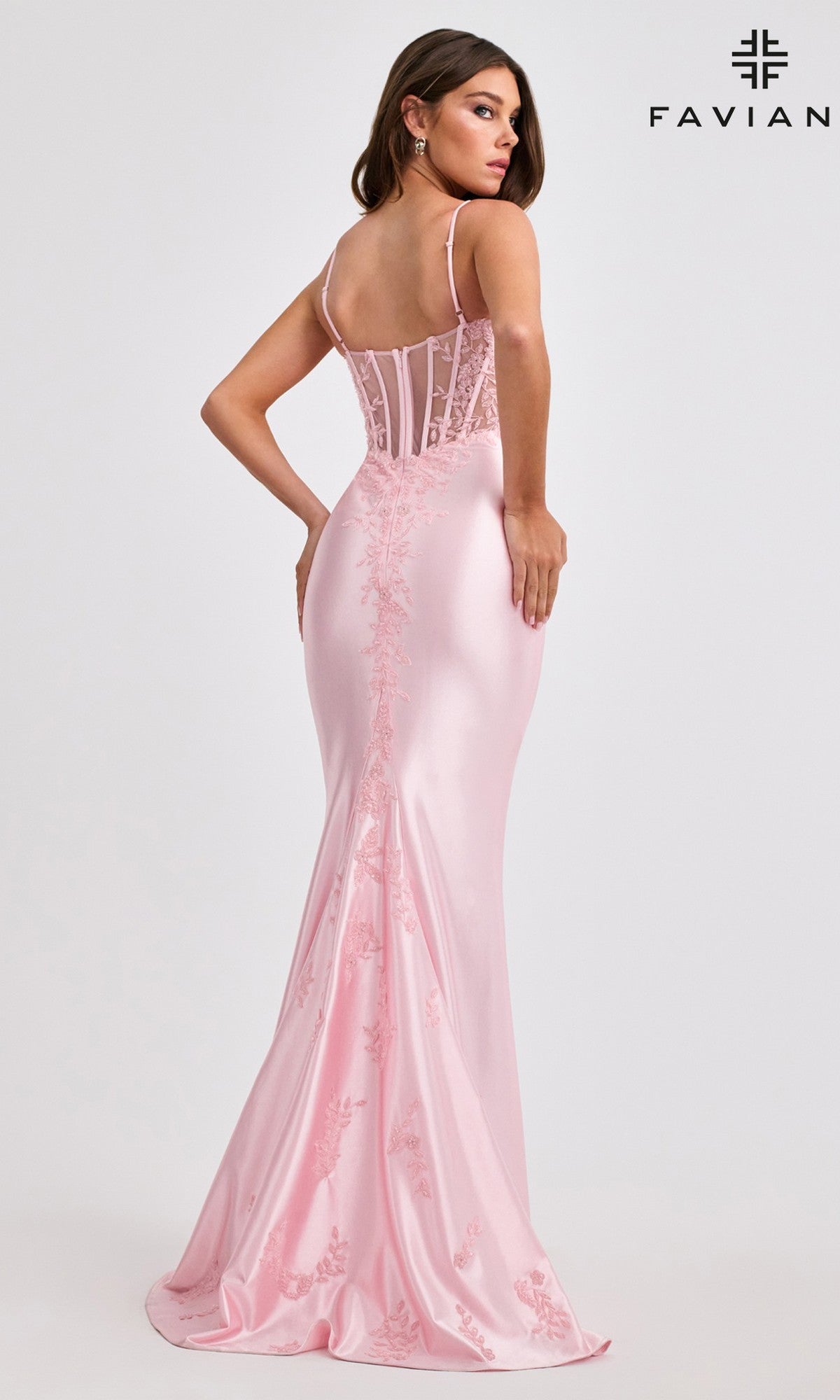 A woman in a pale pink, floor-length Faviana 11466 prom dress with beaded embroidery, delicate lace details, and a semi-sheer fitted bodice stands facing away. The